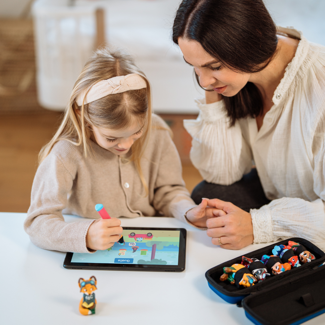 Mutter und Tochter zeichnen auf einem Tablet. Stift und Spielzeug liegen auf dem Tisch.