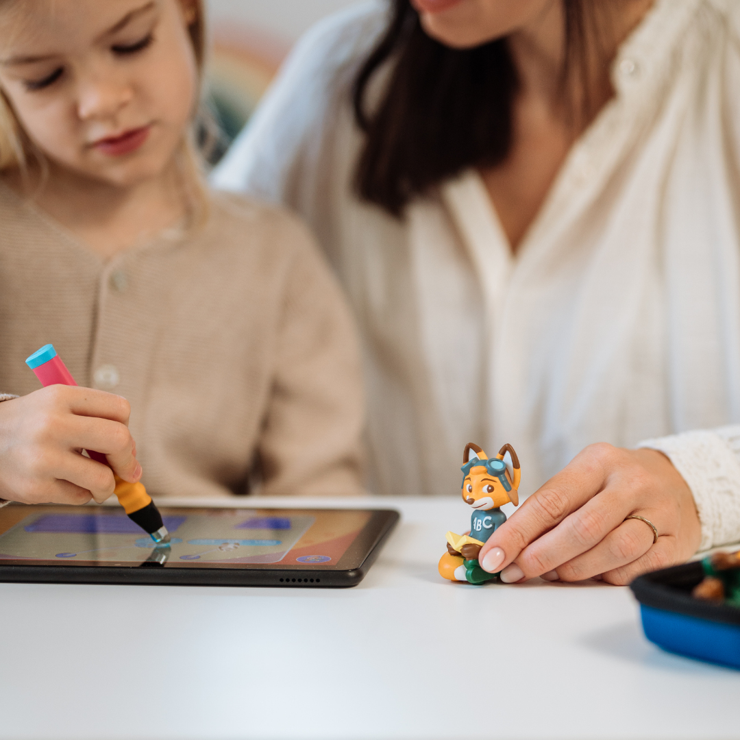 Ein Mädchen und eine Frau zeichnen auf einem Tablet. Ein Fuchspielzeug liegt auf dem Tisch.