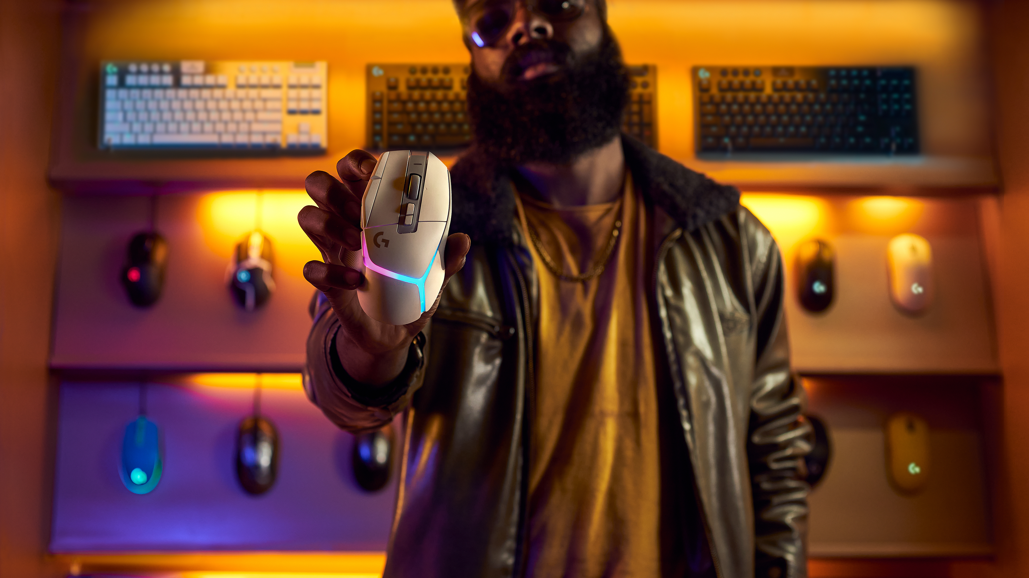 Mężczyzna trzyma białą mysz do gier ze światłami RGB. W tle inne myszy i klawiatury.