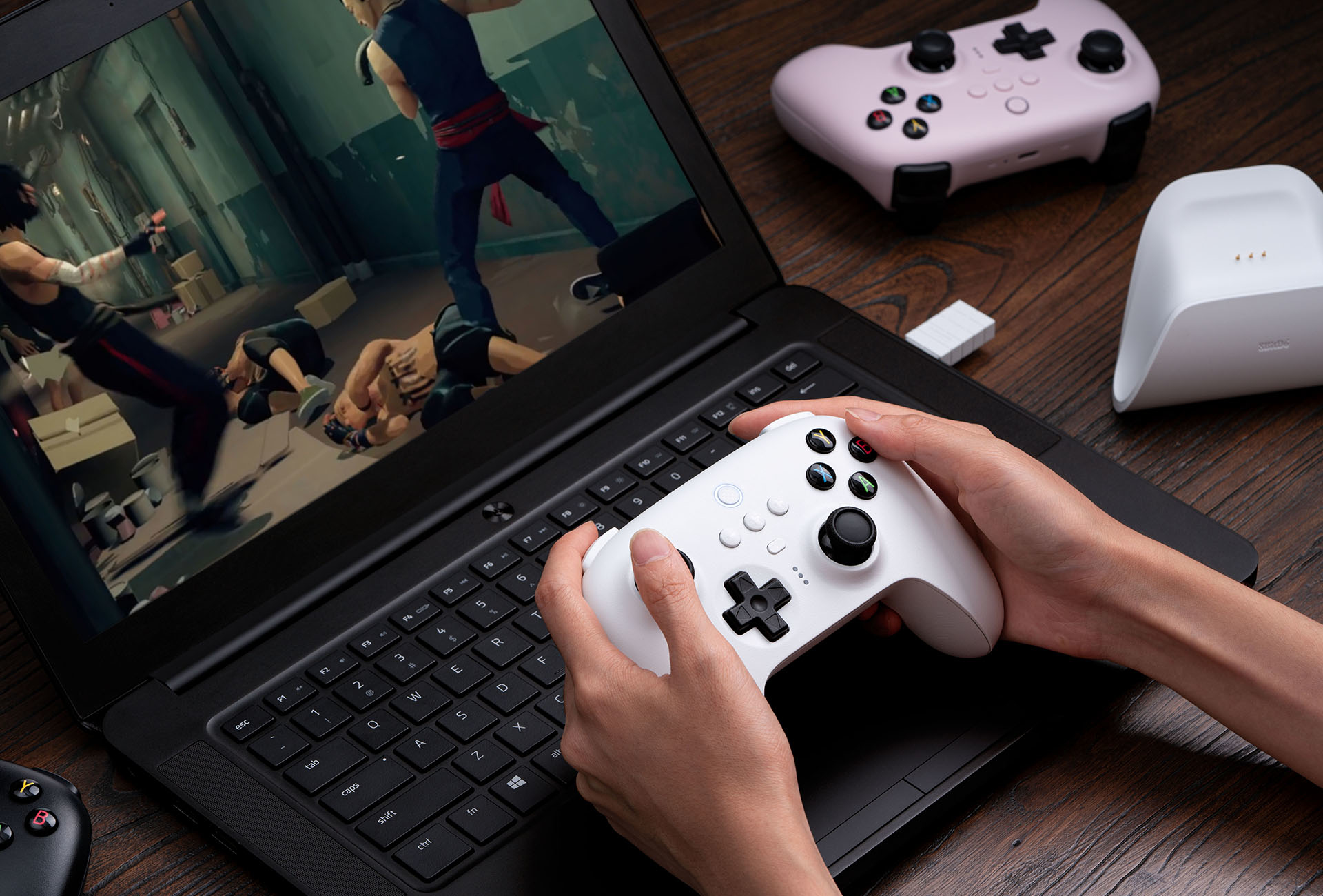 Osoba trzymająca biały kontroler gra w grę na czarnym laptopie.