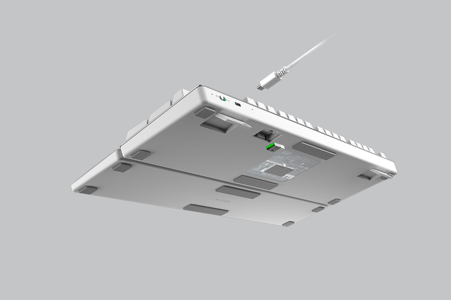 Vue de dessous d'un clavier blanc avec un câble USB branché, sur une surface grise.