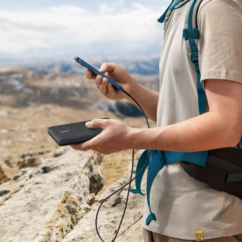 Hombre con teléfono y batería externa. Fondo: montaña.
