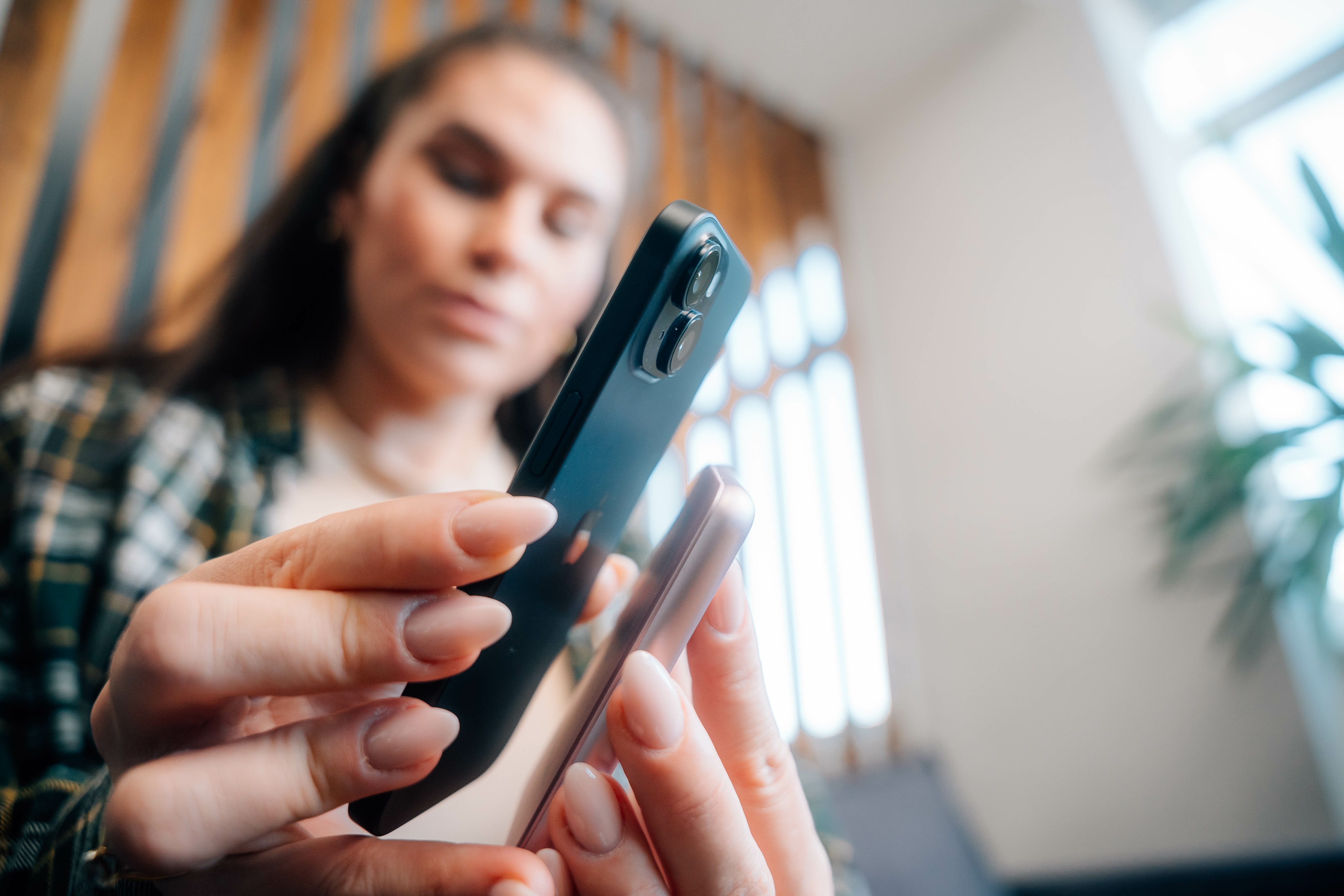 Vrouw die twee telefoons vasthoudt, een zwarte en een lichtroze, op een wazige achtergrond.