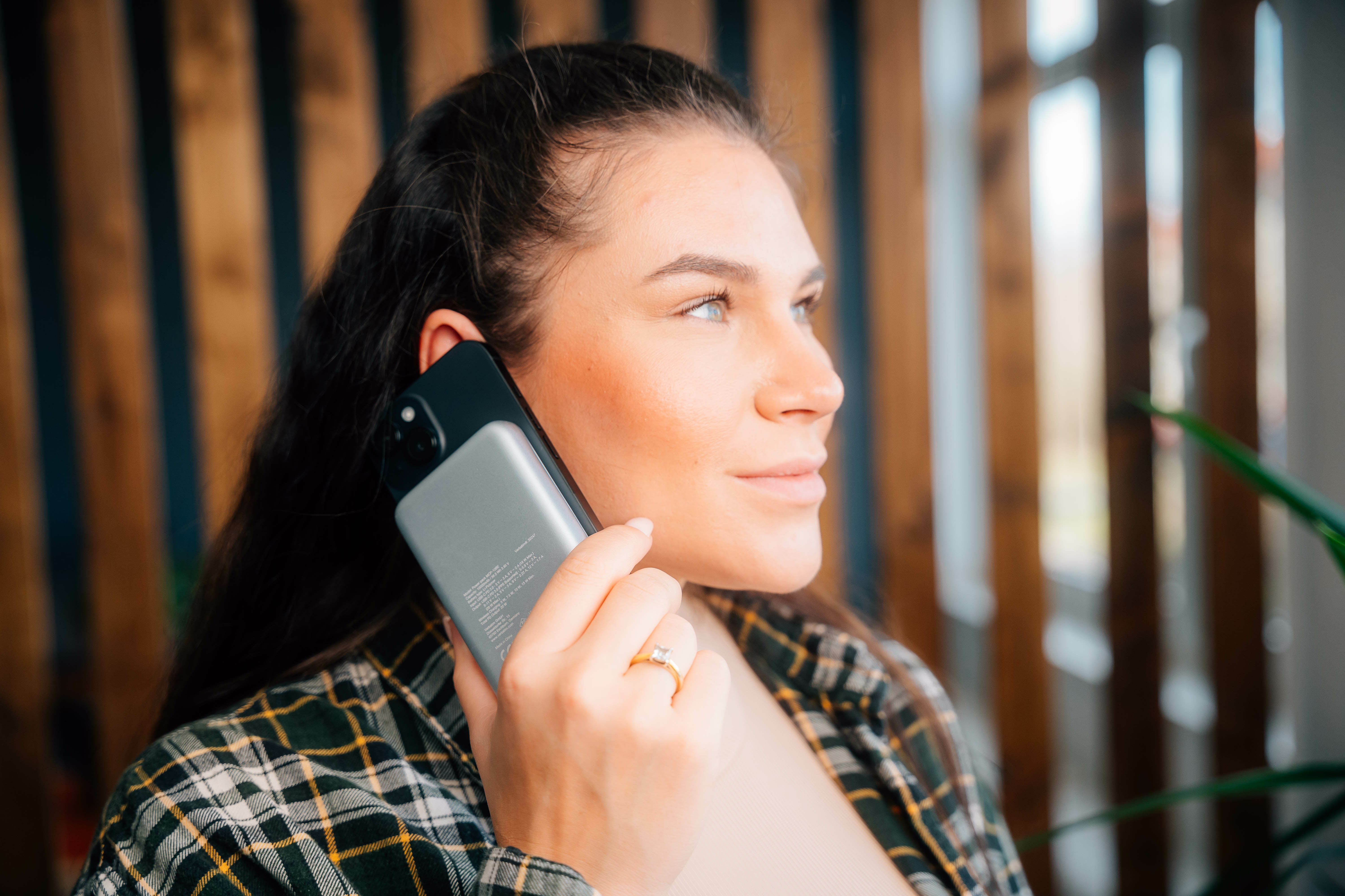 Een vrouw die een zwarte telefoon tegen haar oor houdt. Ze draagt een geruit overhemd.
