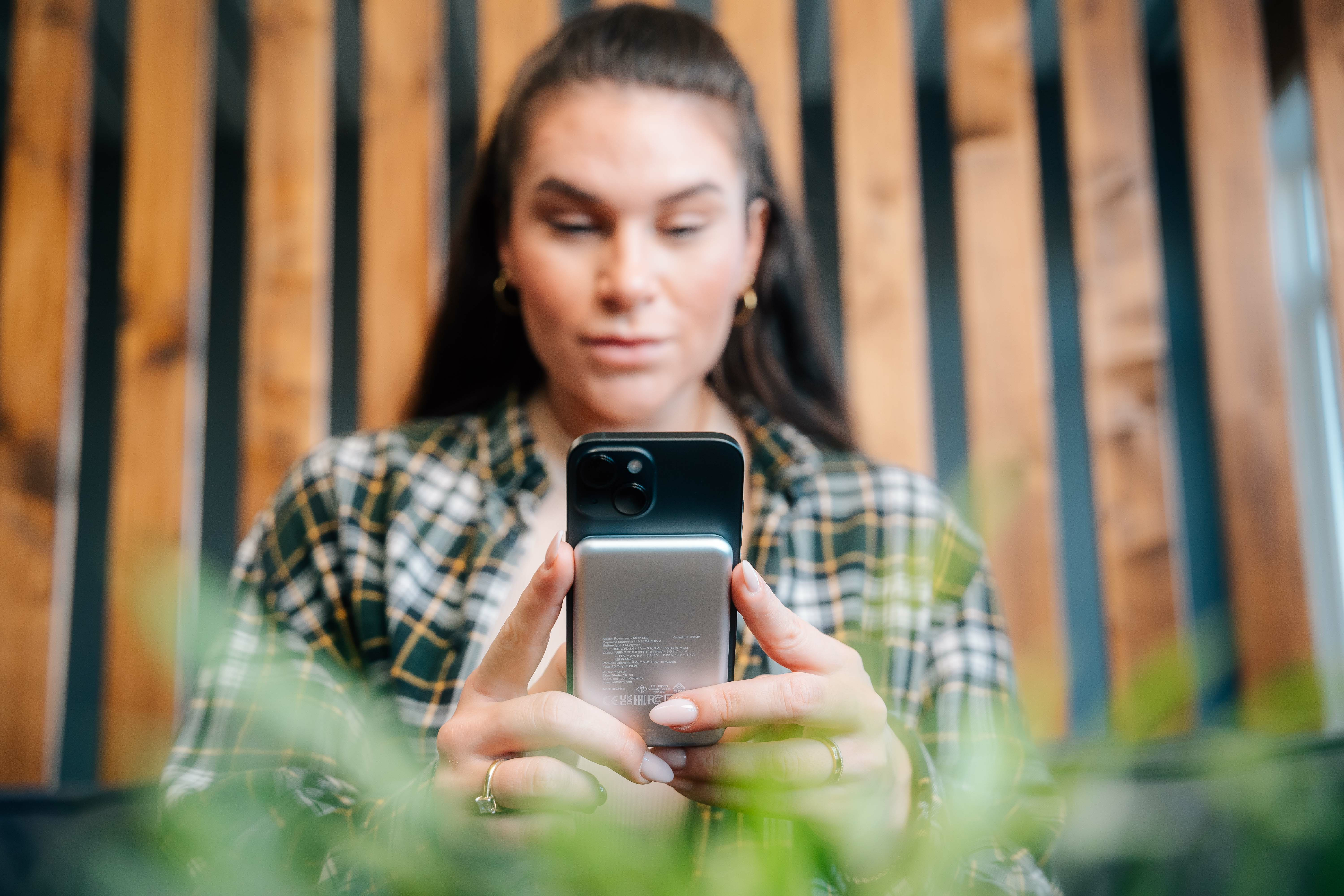 Vrouw houdt een opgevouwen smartphone vast en kijkt naar het scherm. Achtergrond van houten latten.