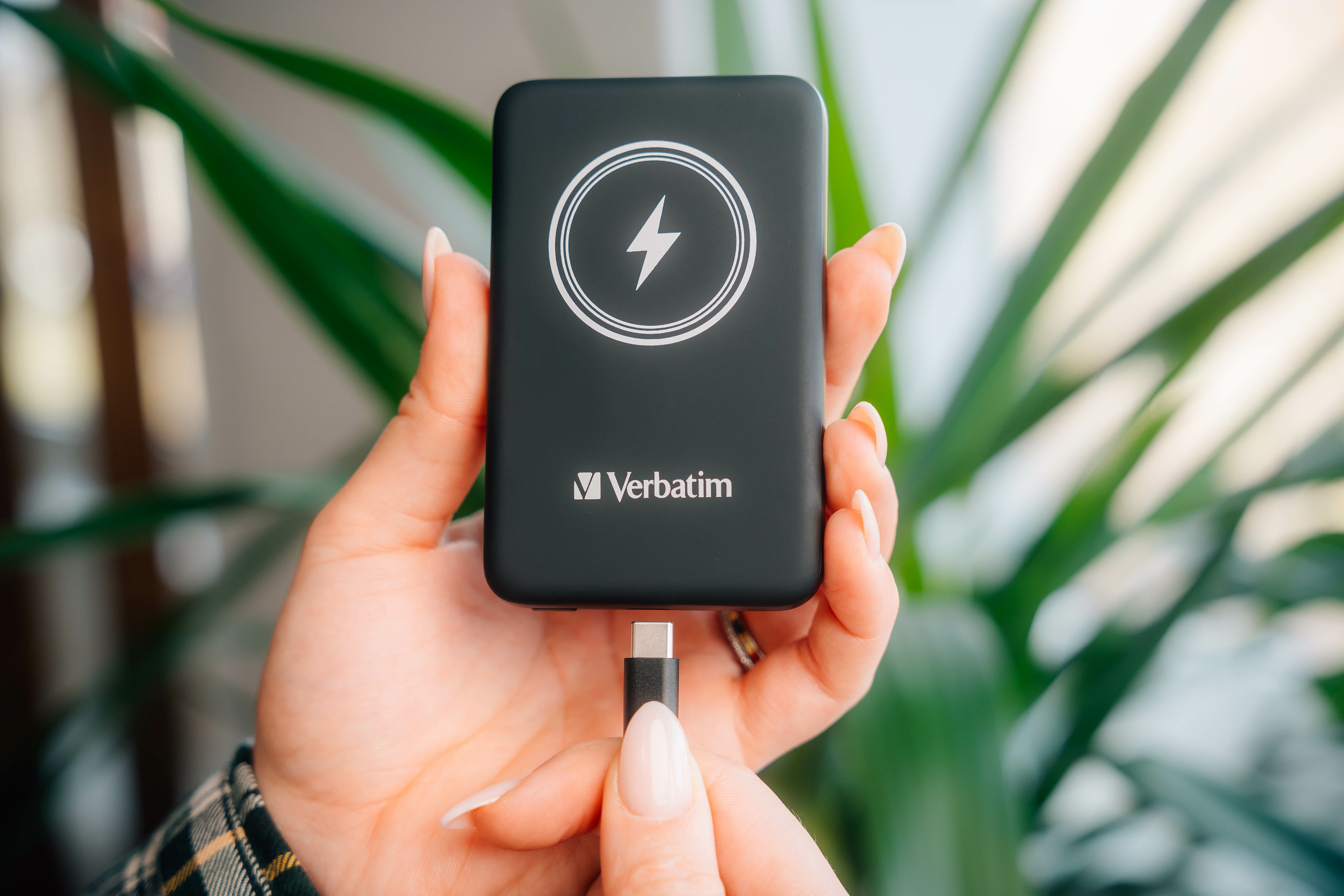 Een hand die een zwarte Verbatim powerbank vasthoudt met een bliksempictogram en een USB-C-kabel.