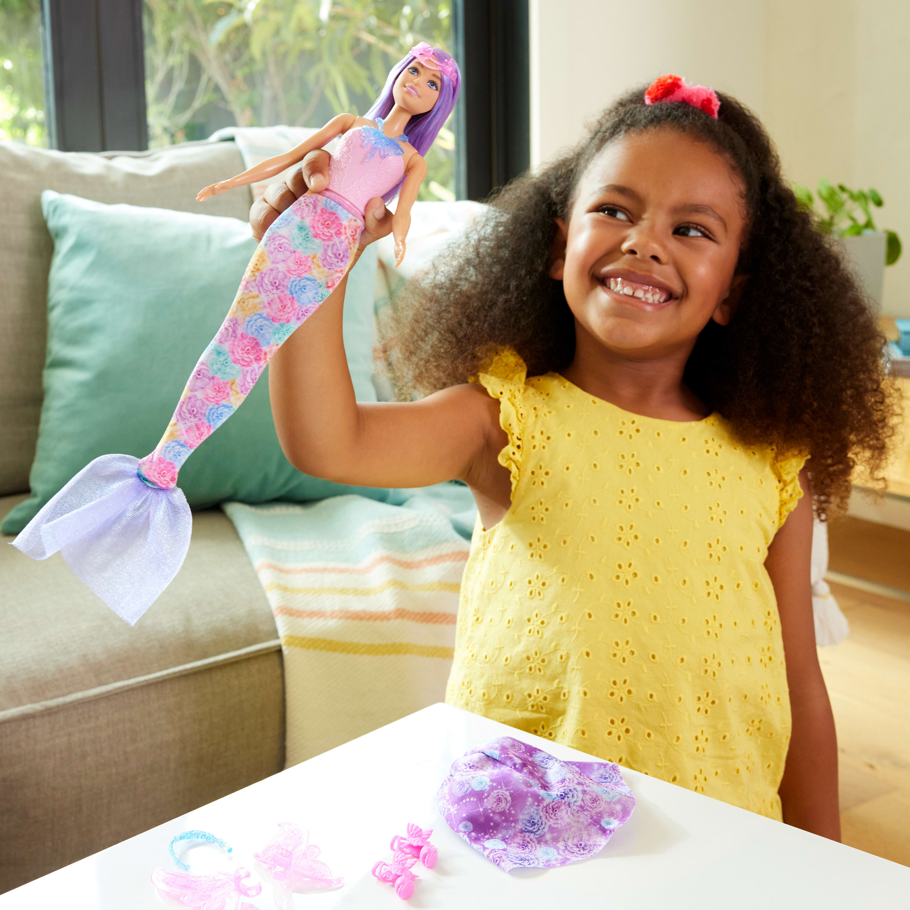 Dziewczynka trzyma lalkę Barbie syrenkę, obok slime i akcesoriów do zabawy.