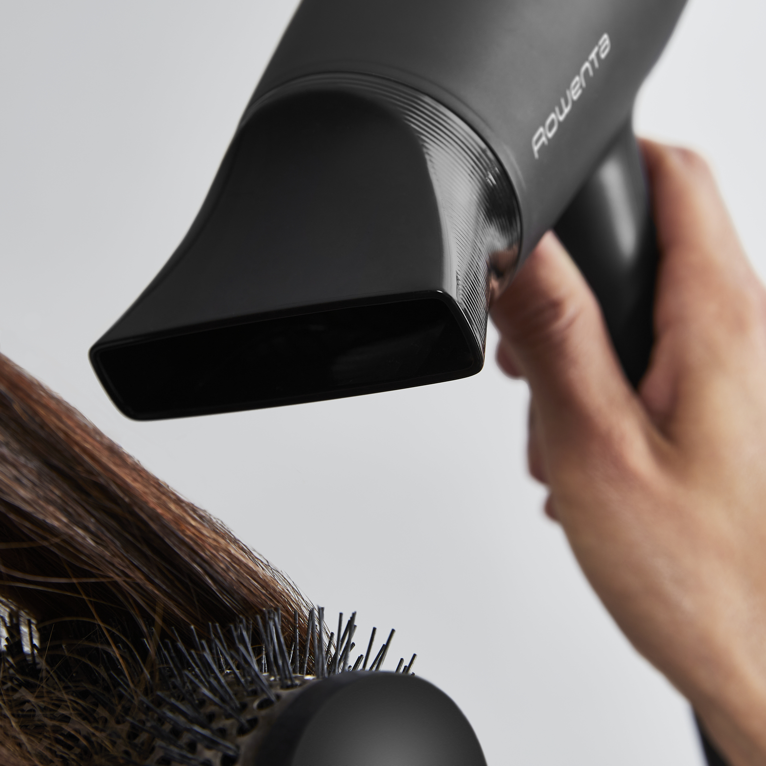 Czarna suszarka do włosów używana na brązowych włosach i okrągła szczotka.