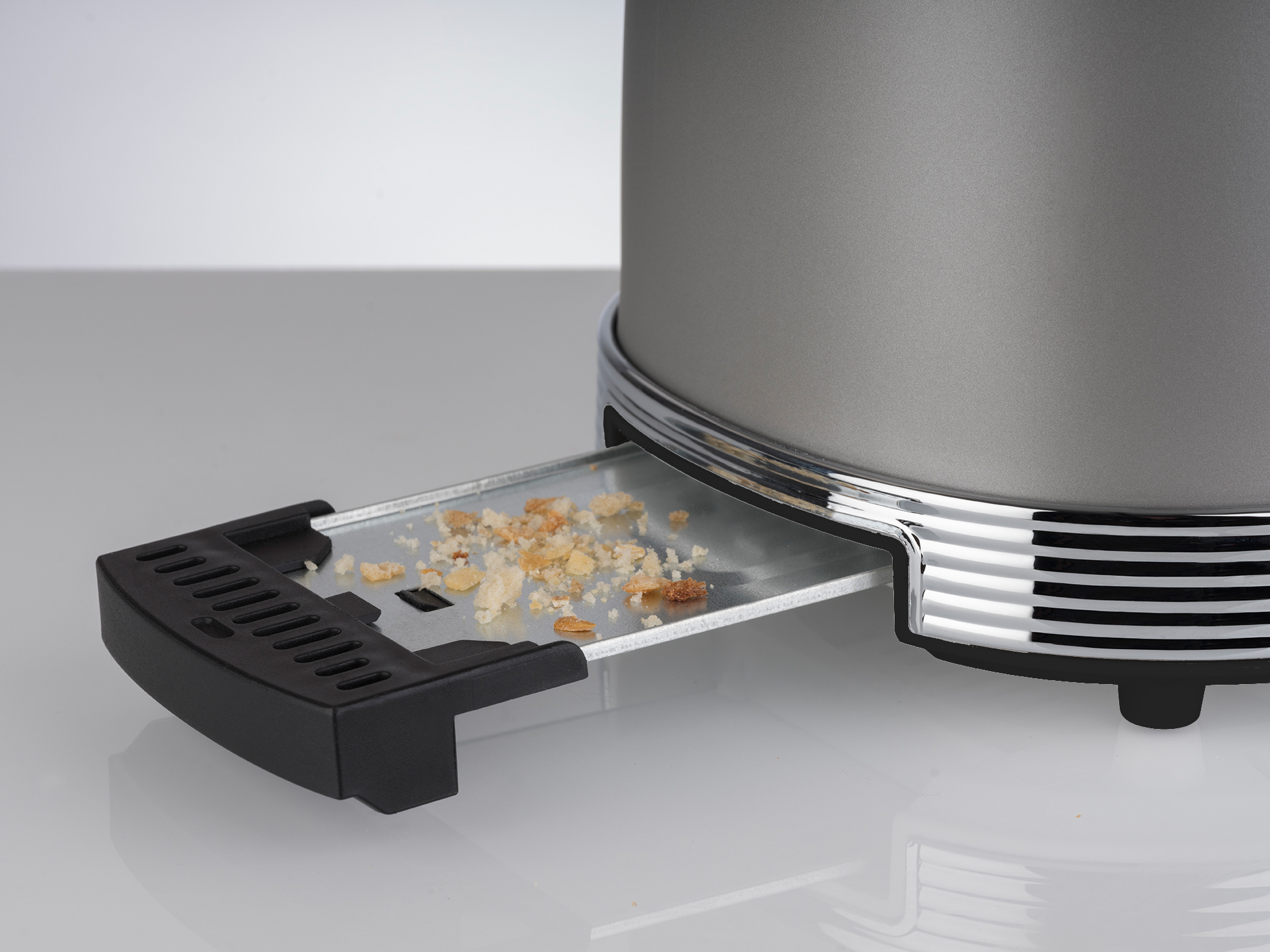 Grauer Toaster mit herausgezogener Krümelschublade, gefüllt mit Brotkrumen. Silberne Zierleisten akzentuieren den Toaster.