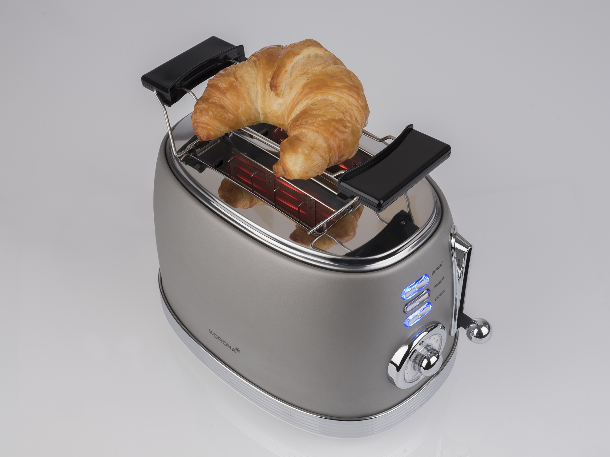 Ein Toaster mit einem Croissant. Der Toaster ist silbergrau und hat Knöpfe für verschiedene Bräunungseinstellungen.
