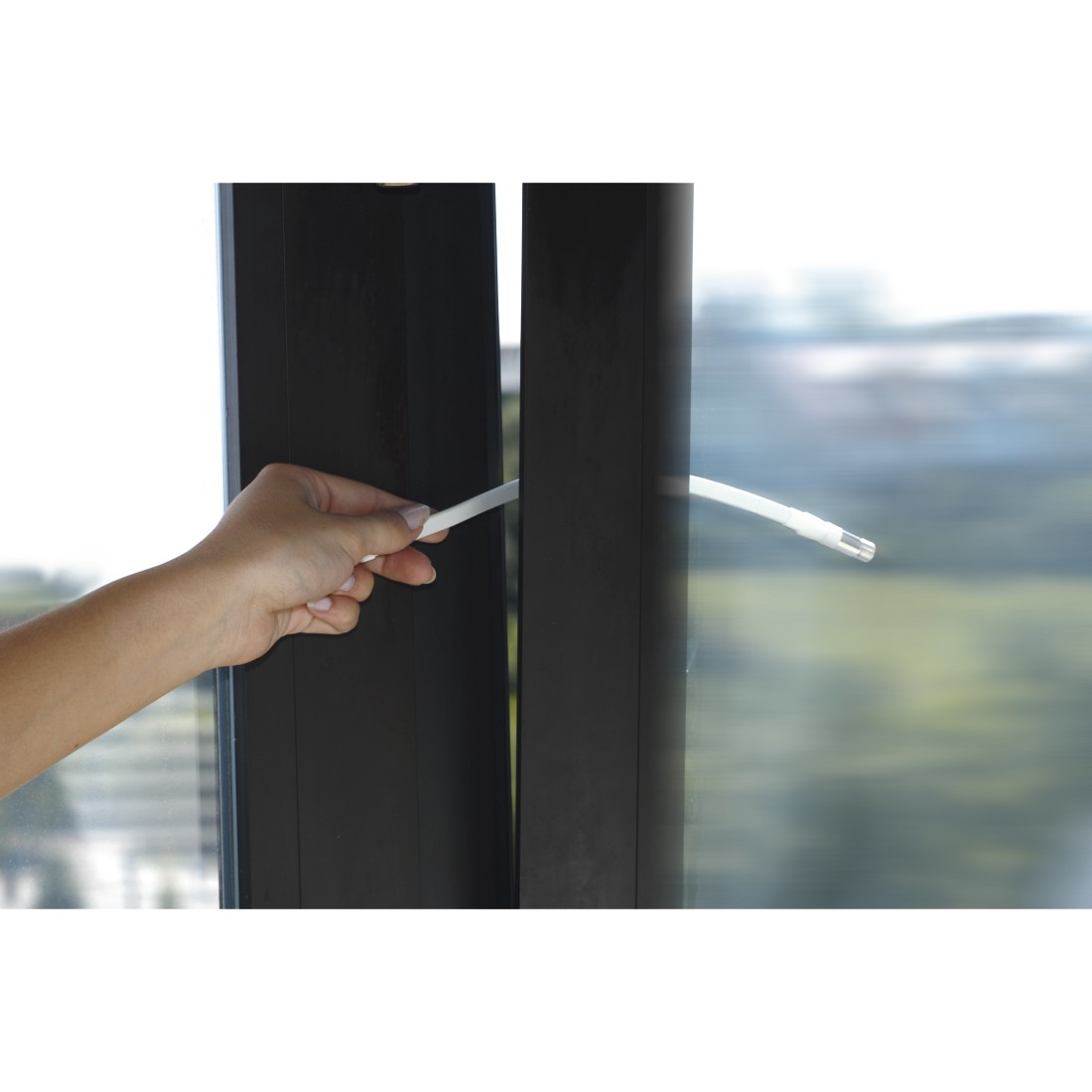 Ręka trzyma białą tubę z uszczelniaczem. Tuba jest między dwiema ramami okien. Tło jest rozmyte.