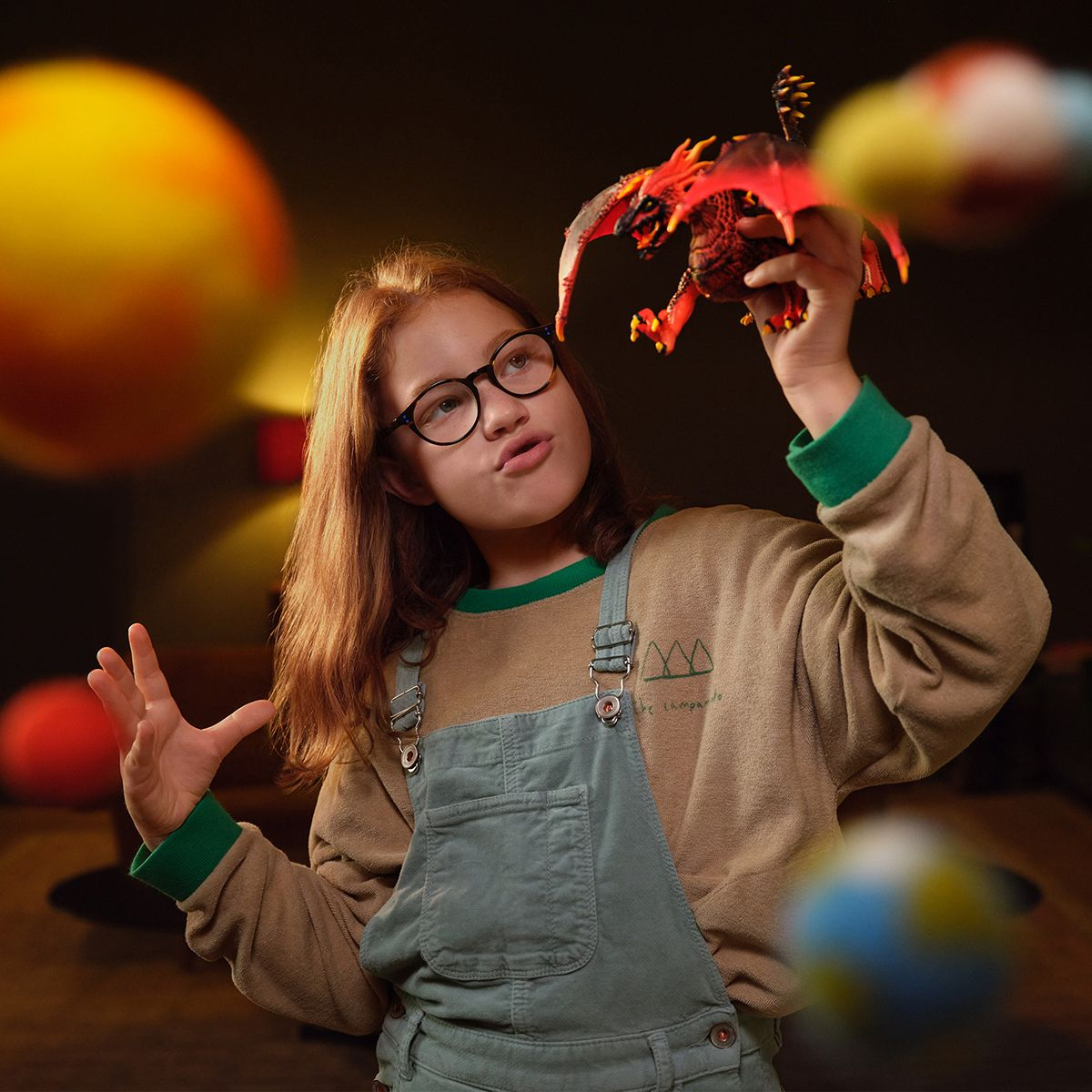Dziewczyna w okularach patrzy na zabawkę smoka, z planetami w tle, w zbliżeniu.