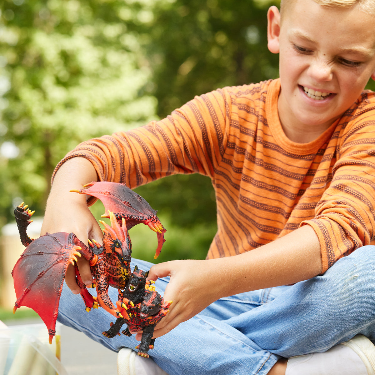 Chłopiec trzyma dwa zabawki smoki. Jeden jest czerwono-czarny, drugi czarny z czerwonym ogonem.