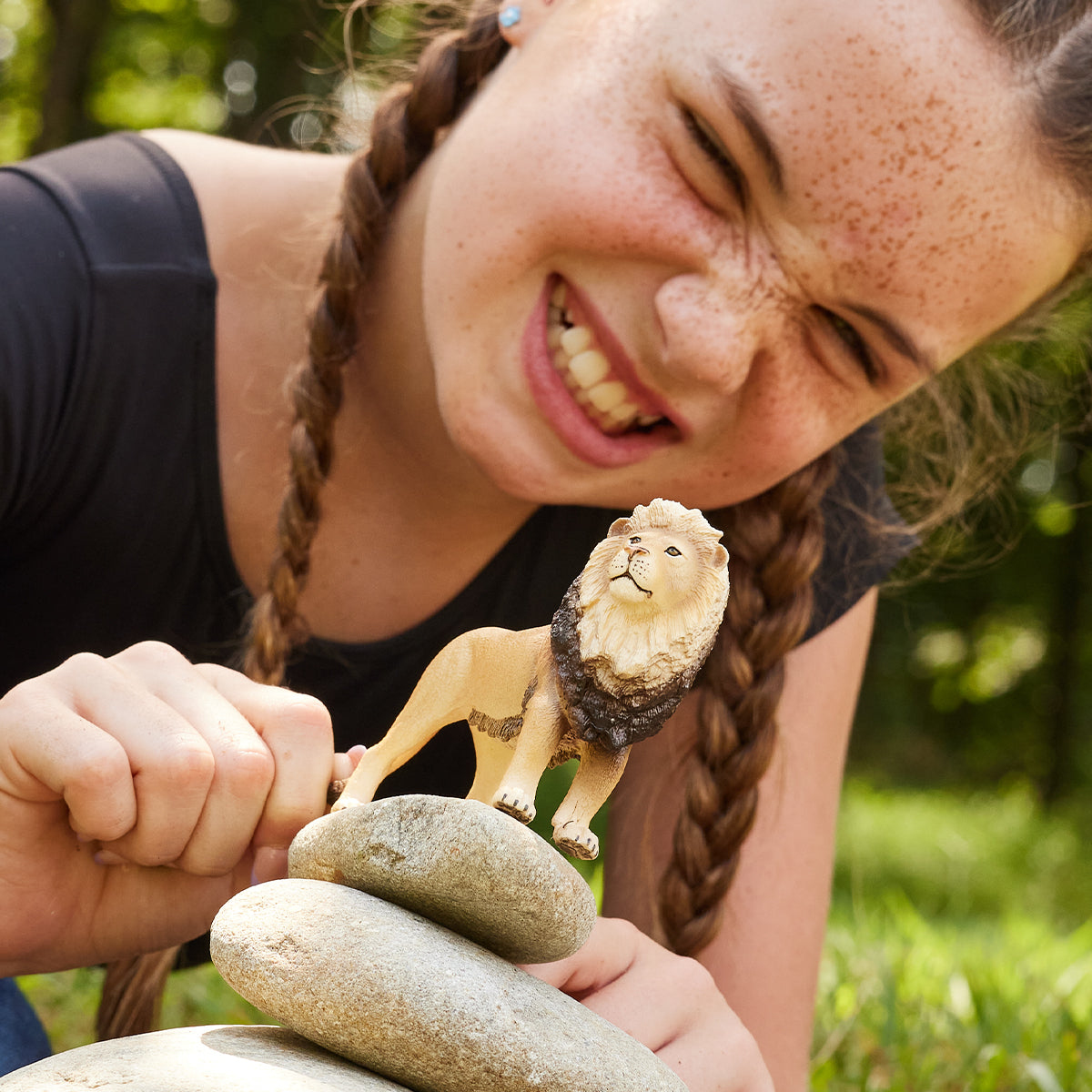 Una bambina tiene un leone giocattolo sulle rocce, sorridendo, con le trecce.