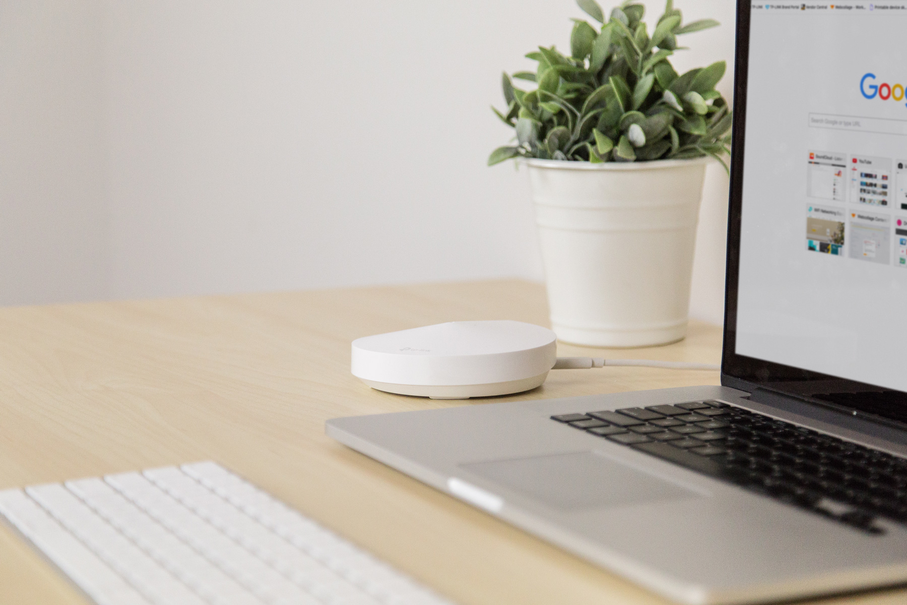 Laptop, biały router i roślina na drewnianym biurku. Google na ekranie laptopa.