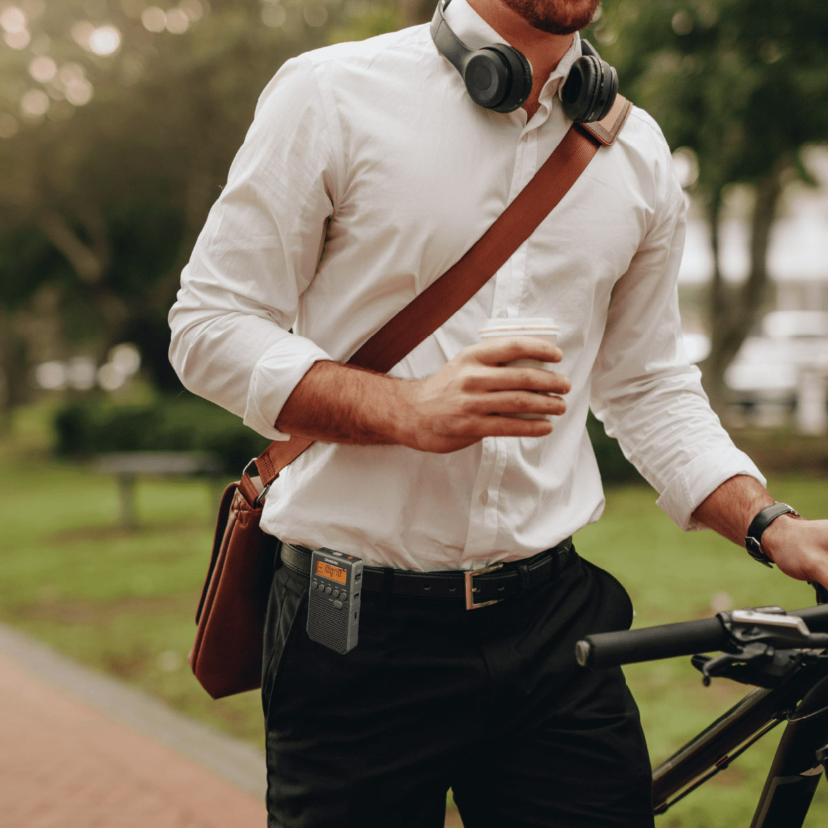 Mężczyzna idący z kawą i torbą, ze słuchawkami i radiem na pasku.