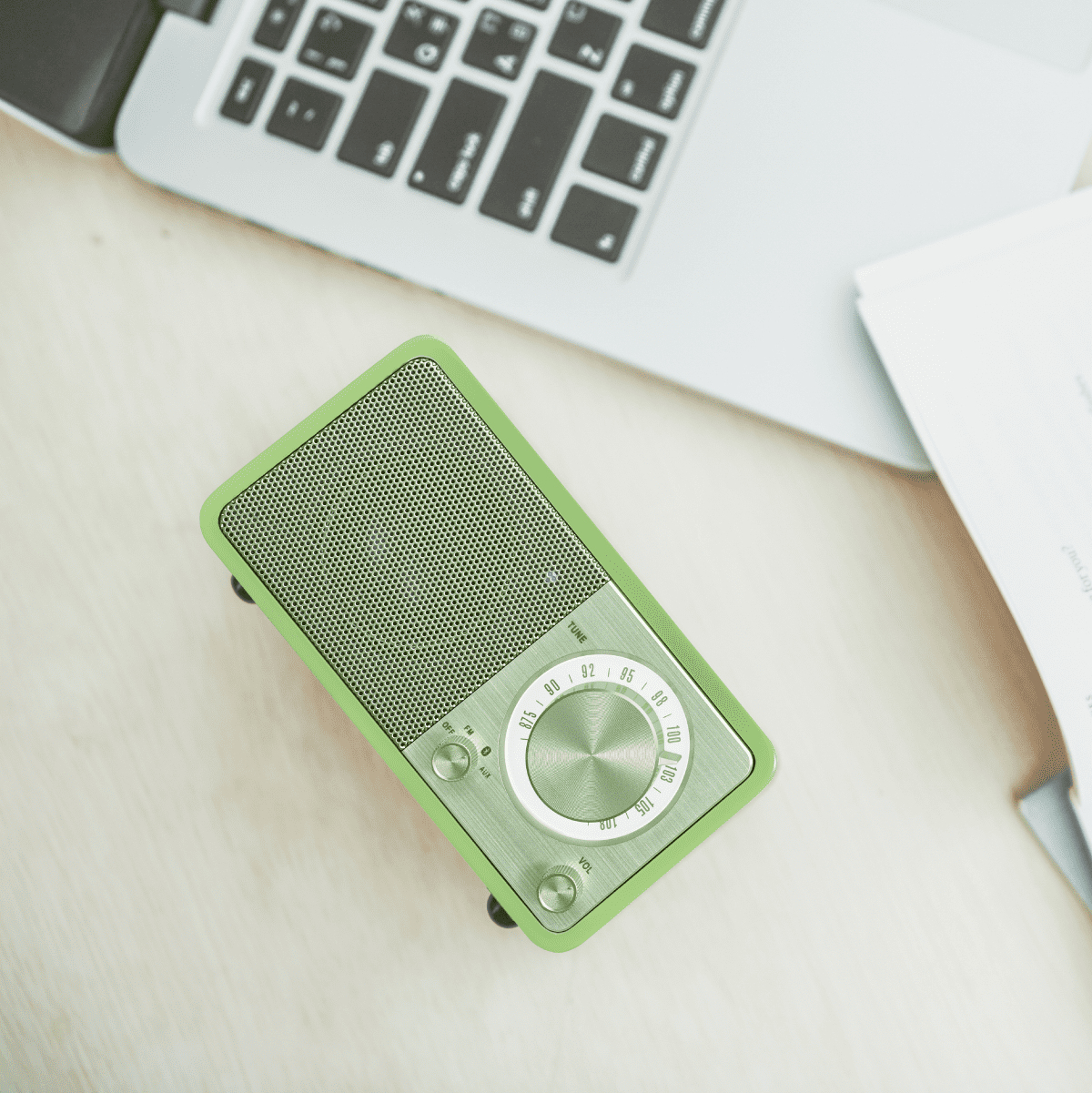 Zielone radio na drewnianej powierzchni obok laptopa. Radio ma pokrętło i przyciski.
