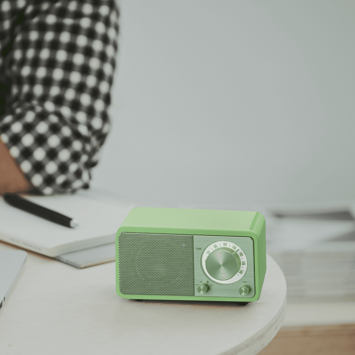Zielone radio retro na stole. Osoba w czarno-białej koszuli w kratę jest częściowo widoczna.