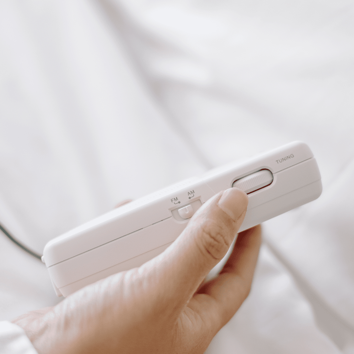 Dłoń trzymająca białe przenośne radio z pokrętłem strojenia i przełącznikiem AM/FM.