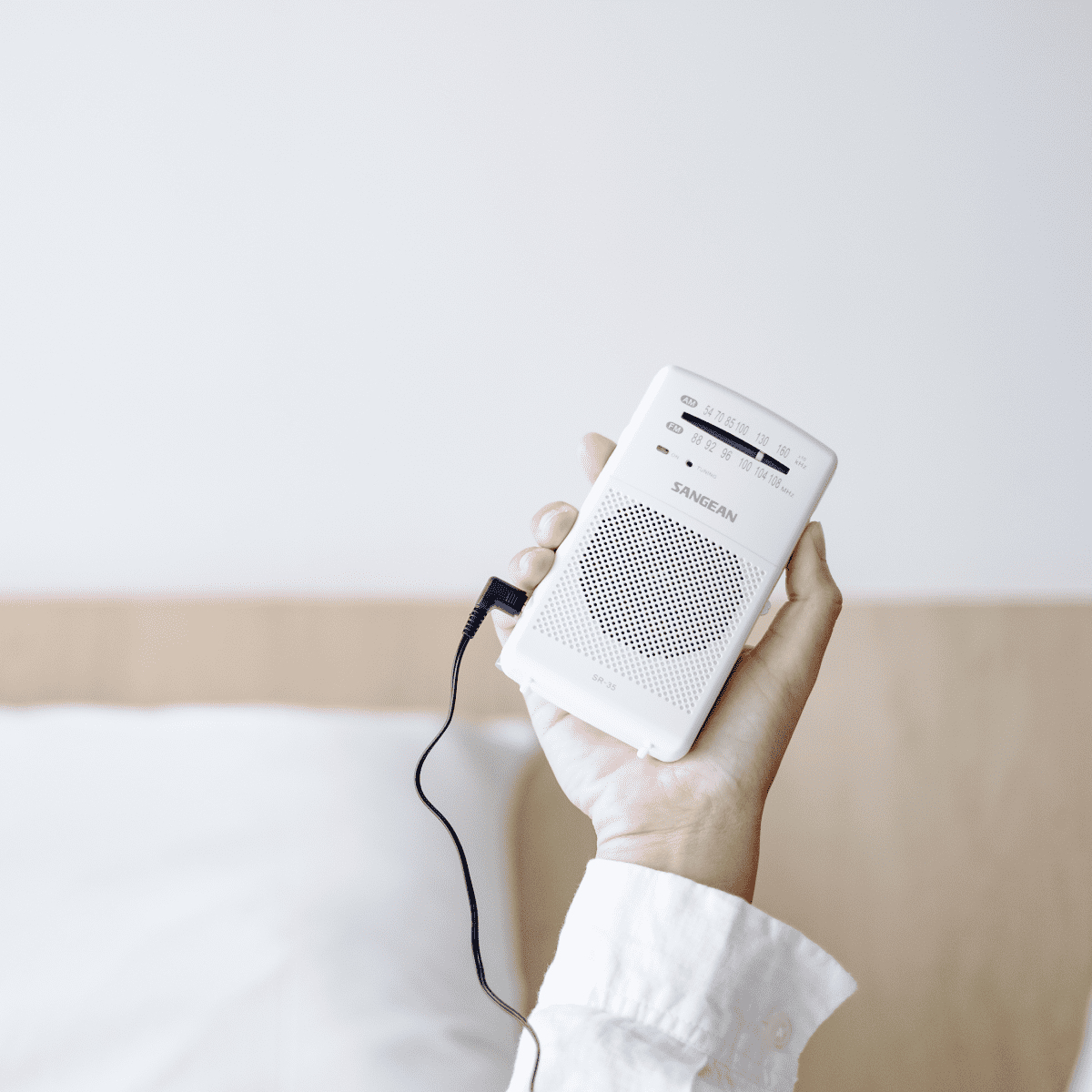 Ręka osoby trzymająca małe białe radio z anteną. Radio ma czarny przewód.