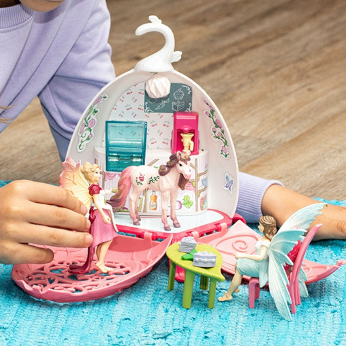 Kind spielt mit einem Feenspielset. Das Set enthält eine Fee, ein Einhorn, einen Tisch, Stühle und eine Kulisse.