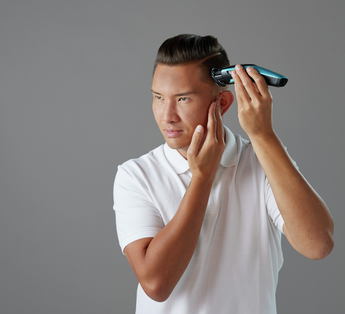 Mężczyzna strzyże włosy czarno-turkusową maszynką.