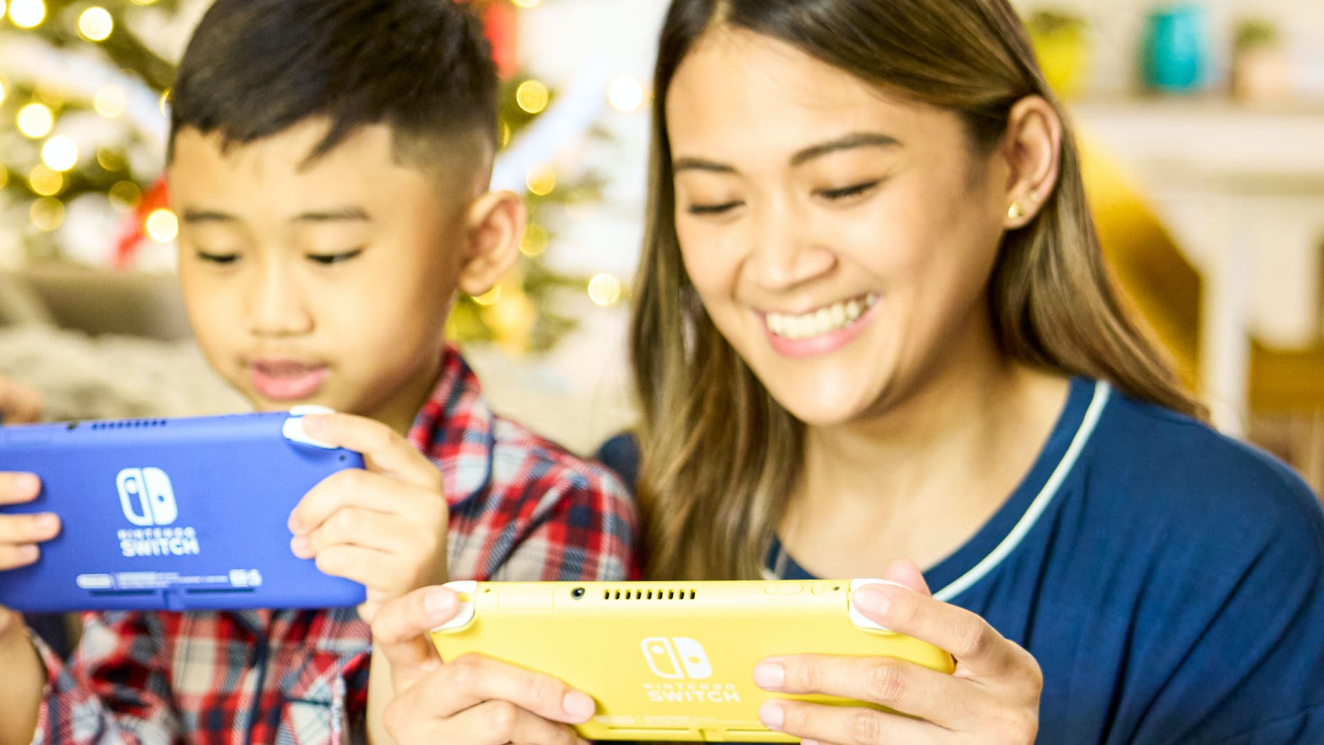Kobieta i chłopiec uśmiechają się i trzymają niebieską i żółtą konsolę Nintendo Switch Lite.
