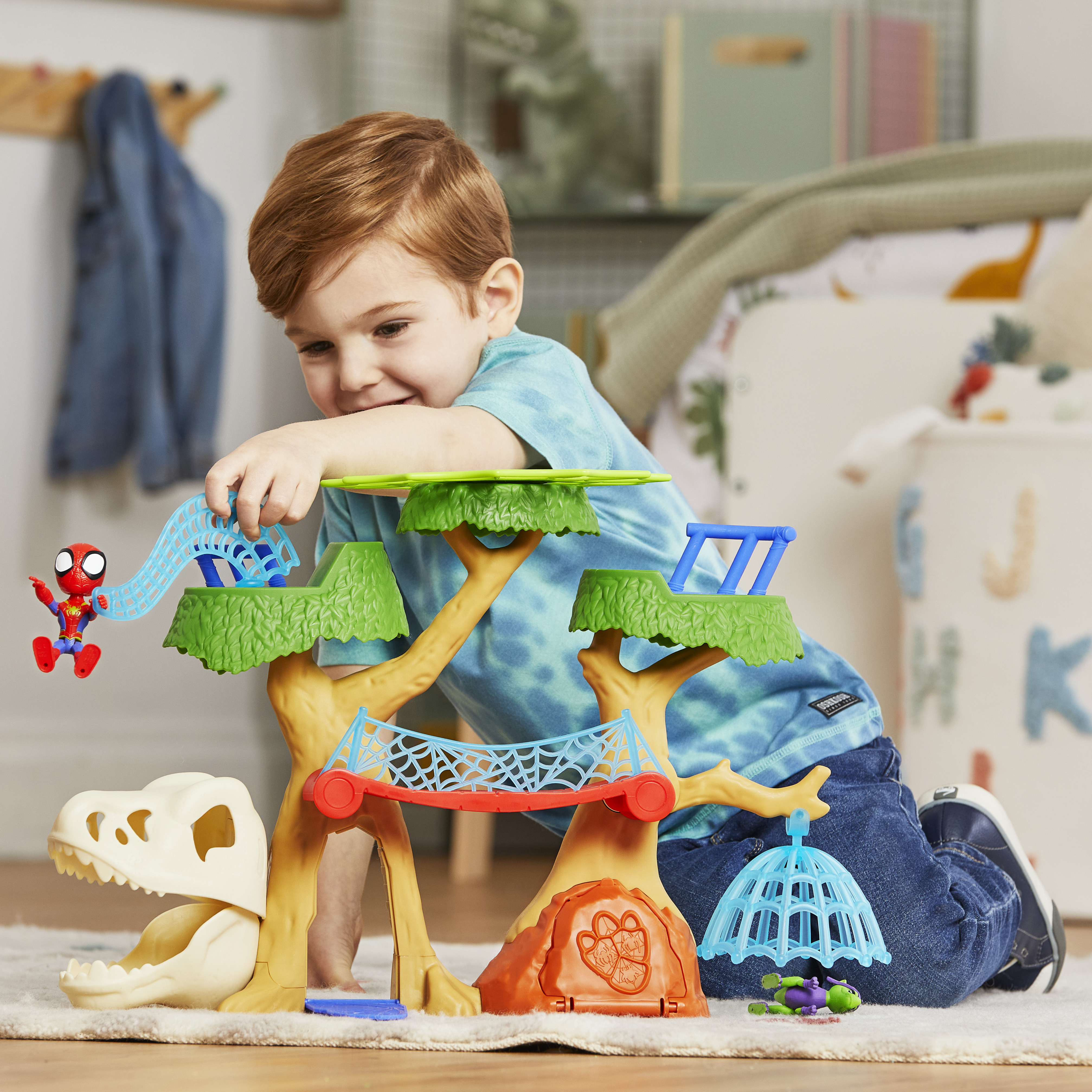 Un bambino gioca con un set di giocattoli a tema dinosauri. Include uno scivolo e una figura di Spiderman.