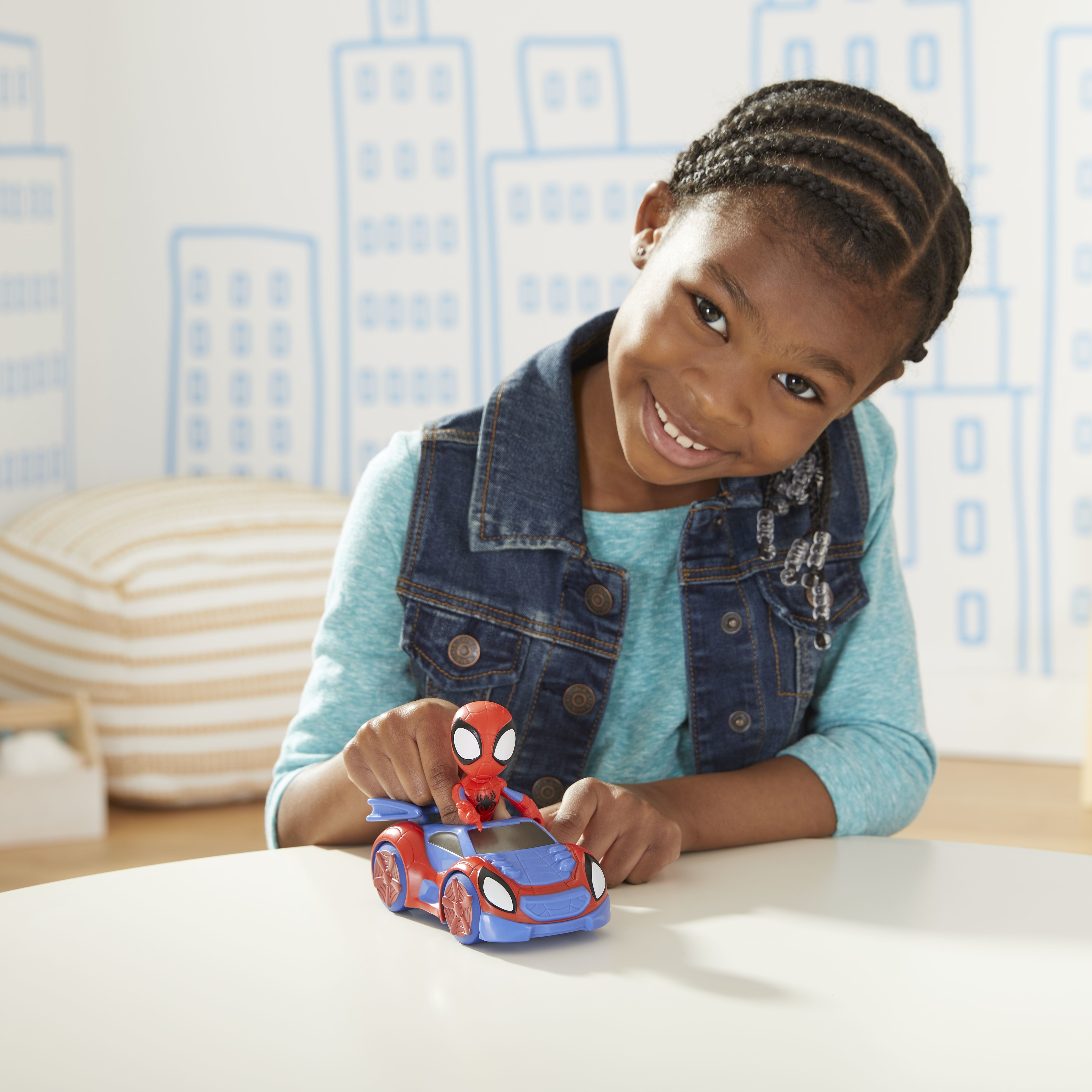 Una niña sonríe mientras juega con un coche de juguete de Spider-Man. El coche y la figura son rojos y azules.