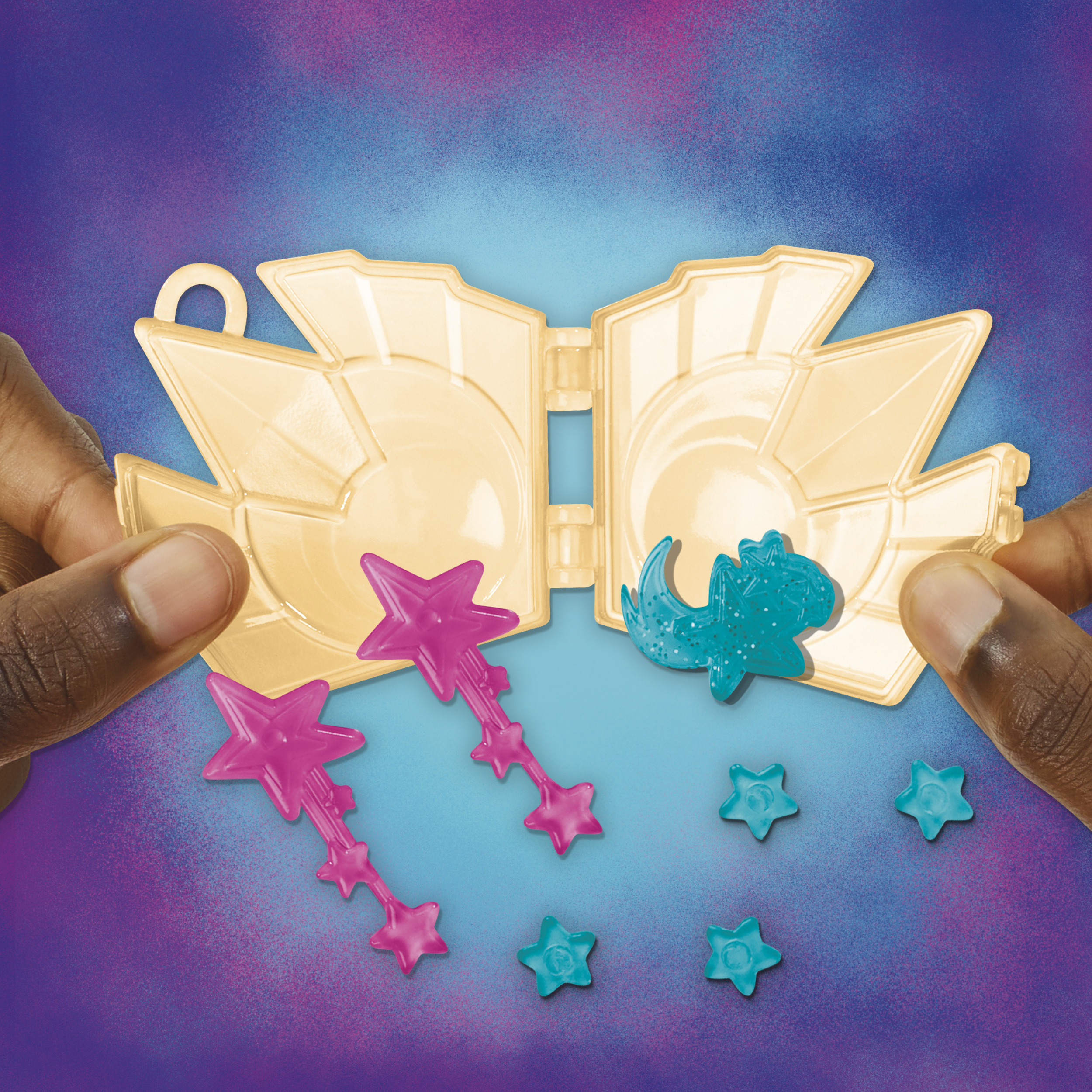 Ręce trzymają otwartą, złotą zabawkę w kształcie skrzydeł z różowymi i niebieskimi akcesoriami w kształcie gwiazd.