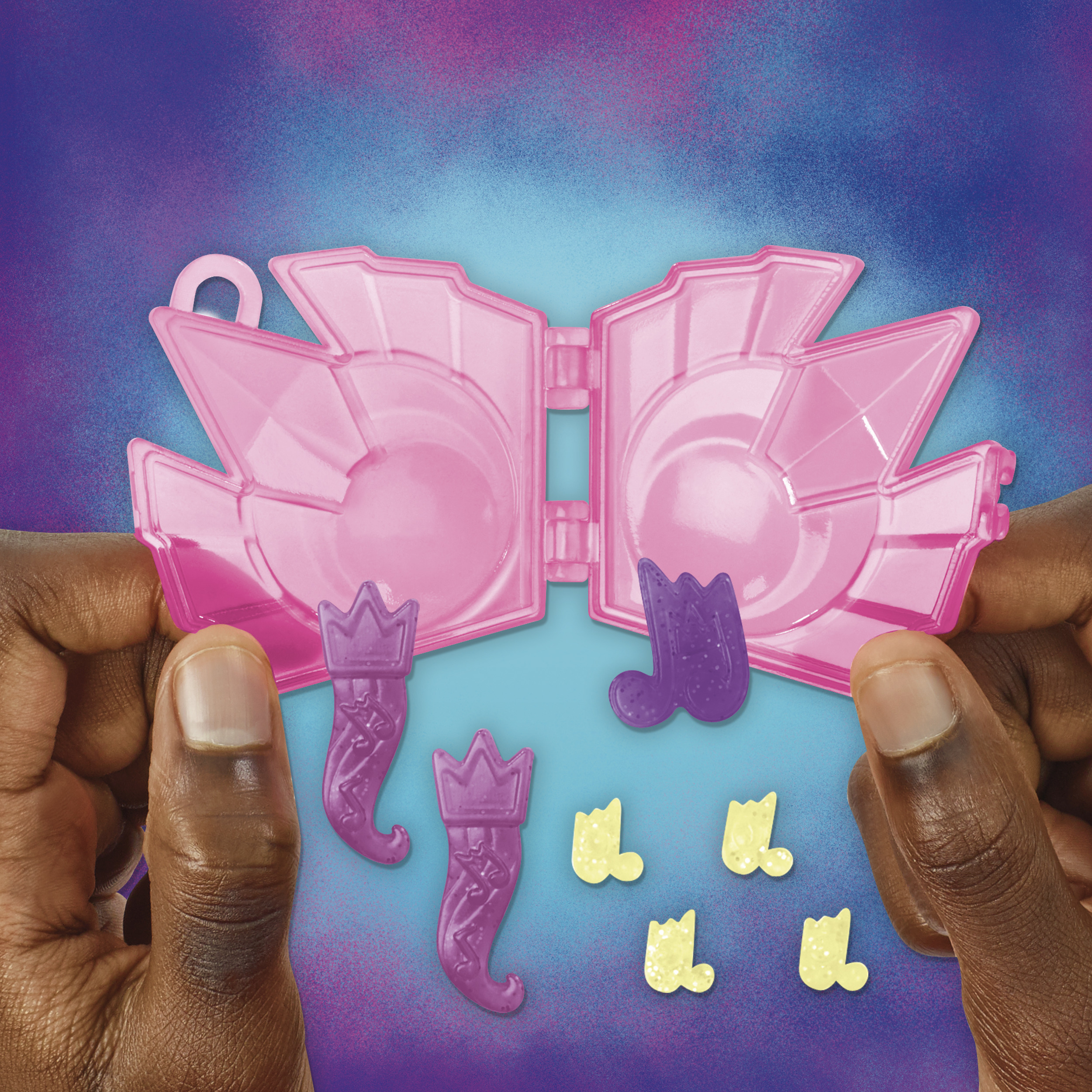 Dłonie trzymające otwartą różową zabawkę. Różowe, fioletowe i żółte akcesoria. Fioletowe tło.