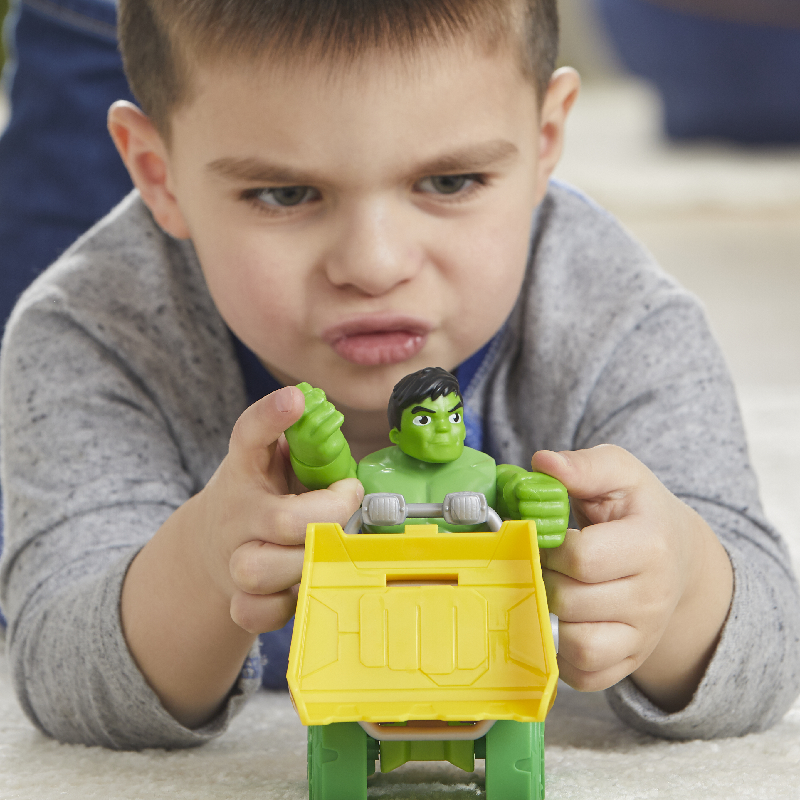 Ein Junge spielt mit einem Hulk-Spielzeug-Truck. Er schaut ihn mit konzentriertem Blick an.