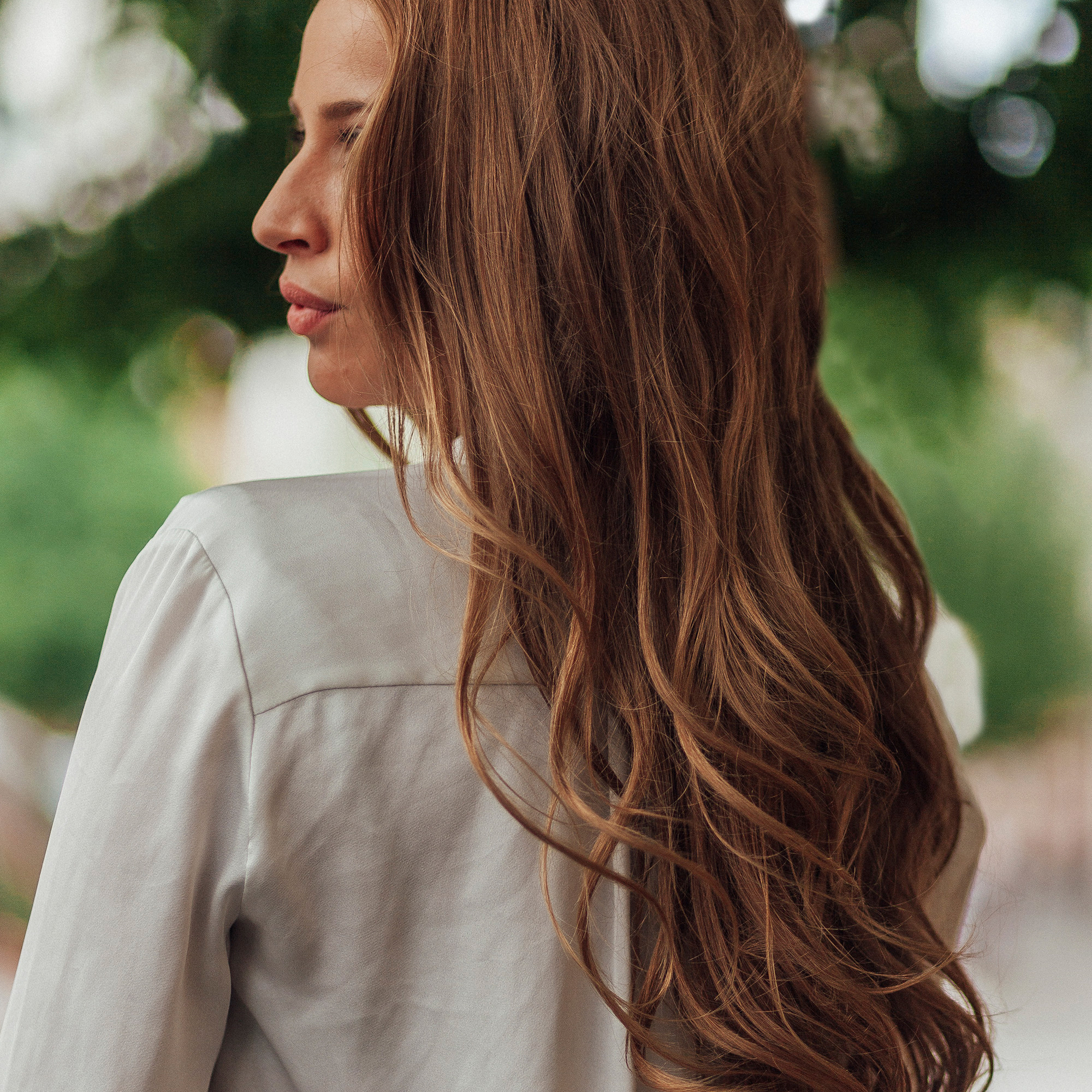 Een vrouw met lang golvend rossig haar van achteren gezien, draagt een wit shirt.