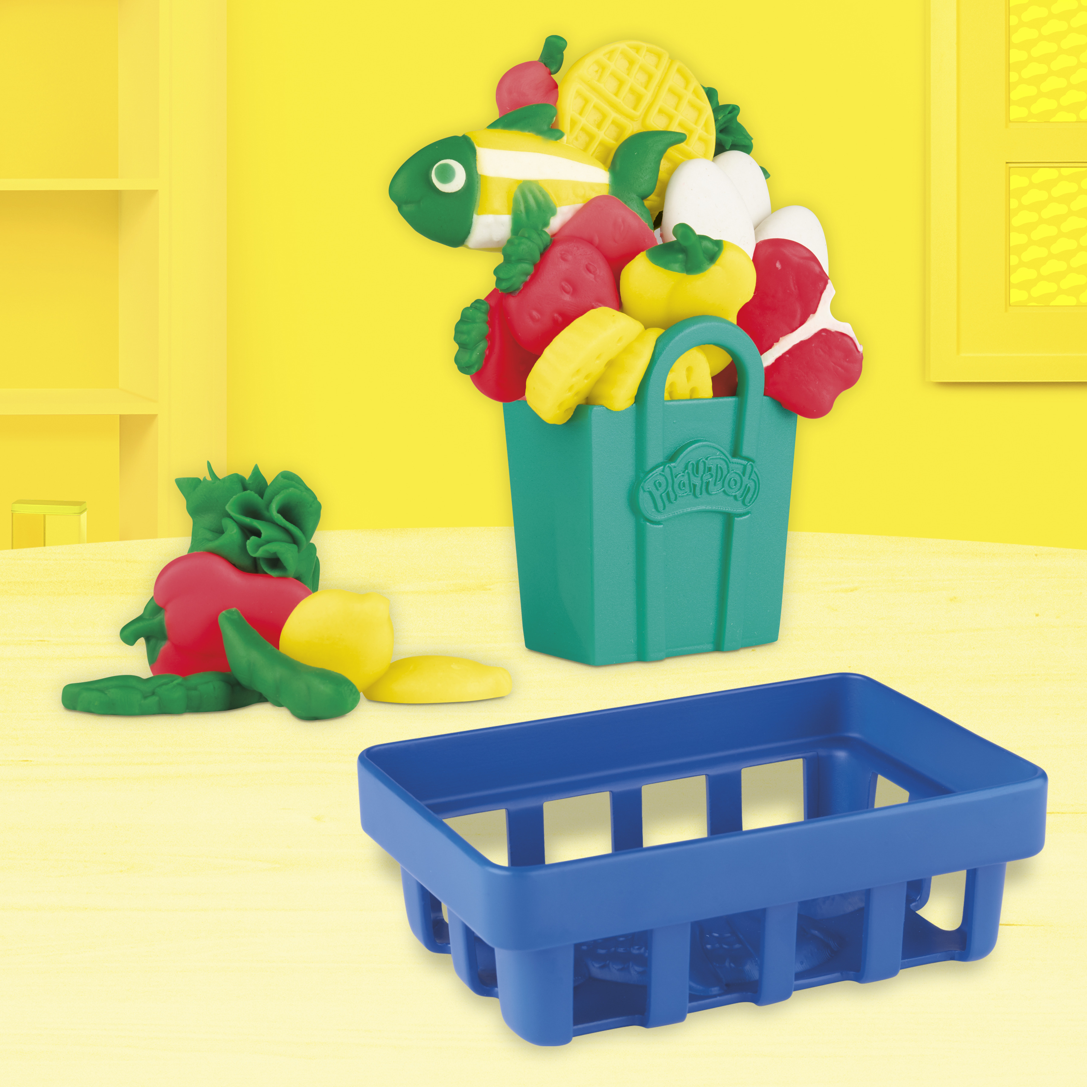 Frutas y verduras Play-Doh en una cesta verde y una azul sobre una superficie amarilla.