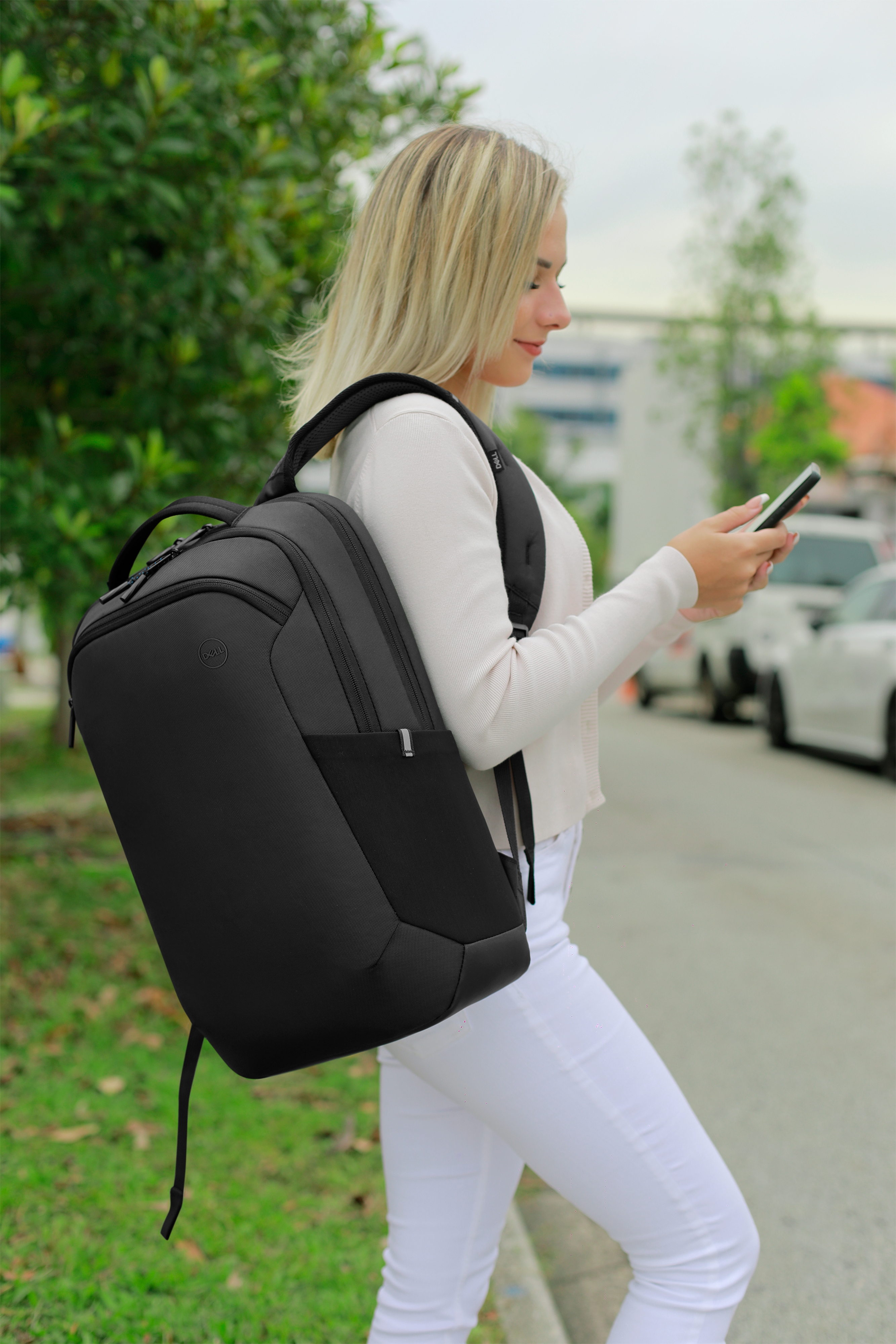 Blonde Frau mit einem schwarzen Rucksack, die ein Telefon benutzt. Straßenhintergrund.