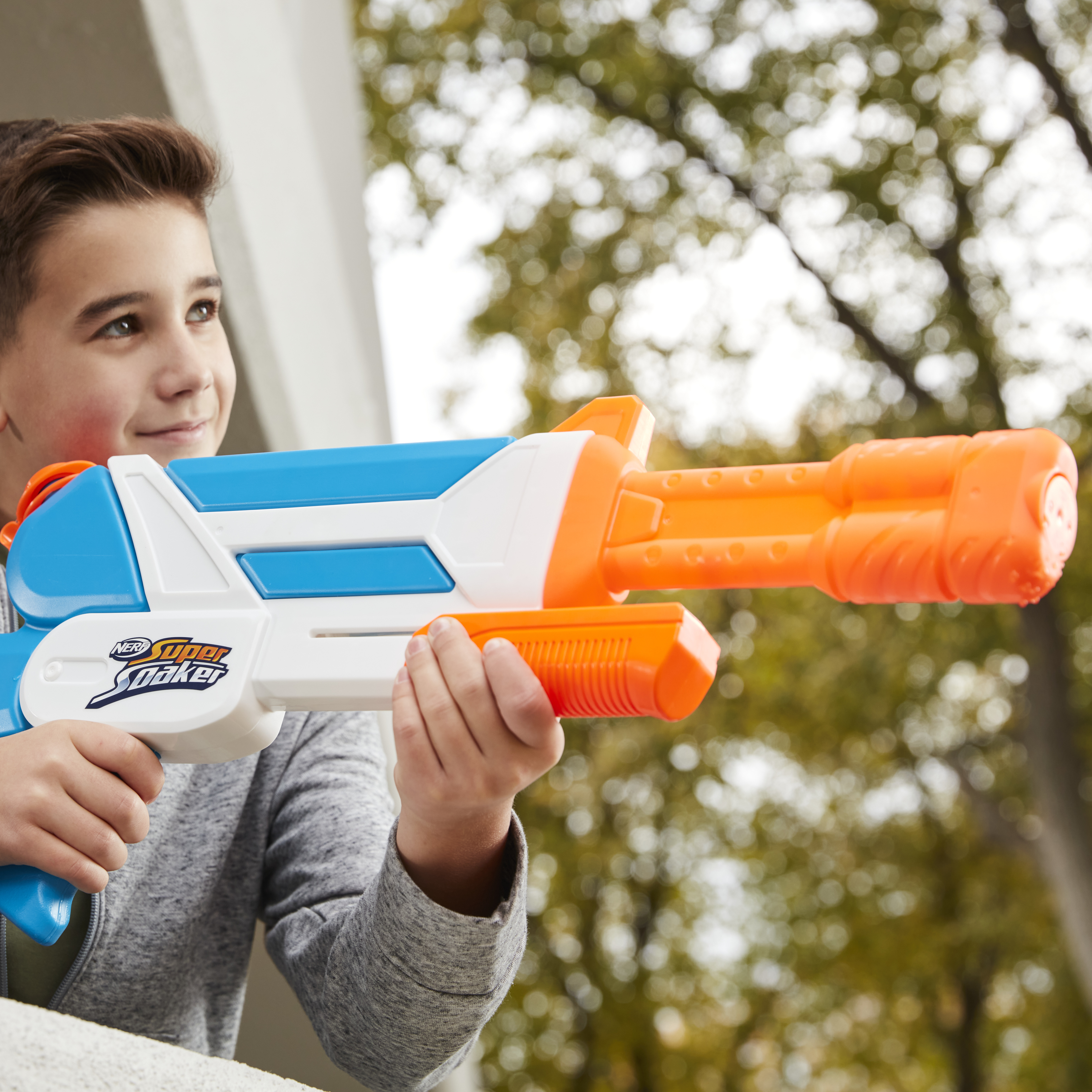Un niño apuntando con una pistola de agua Nerf. La pistola es azul, blanca y naranja. Está al aire libre.