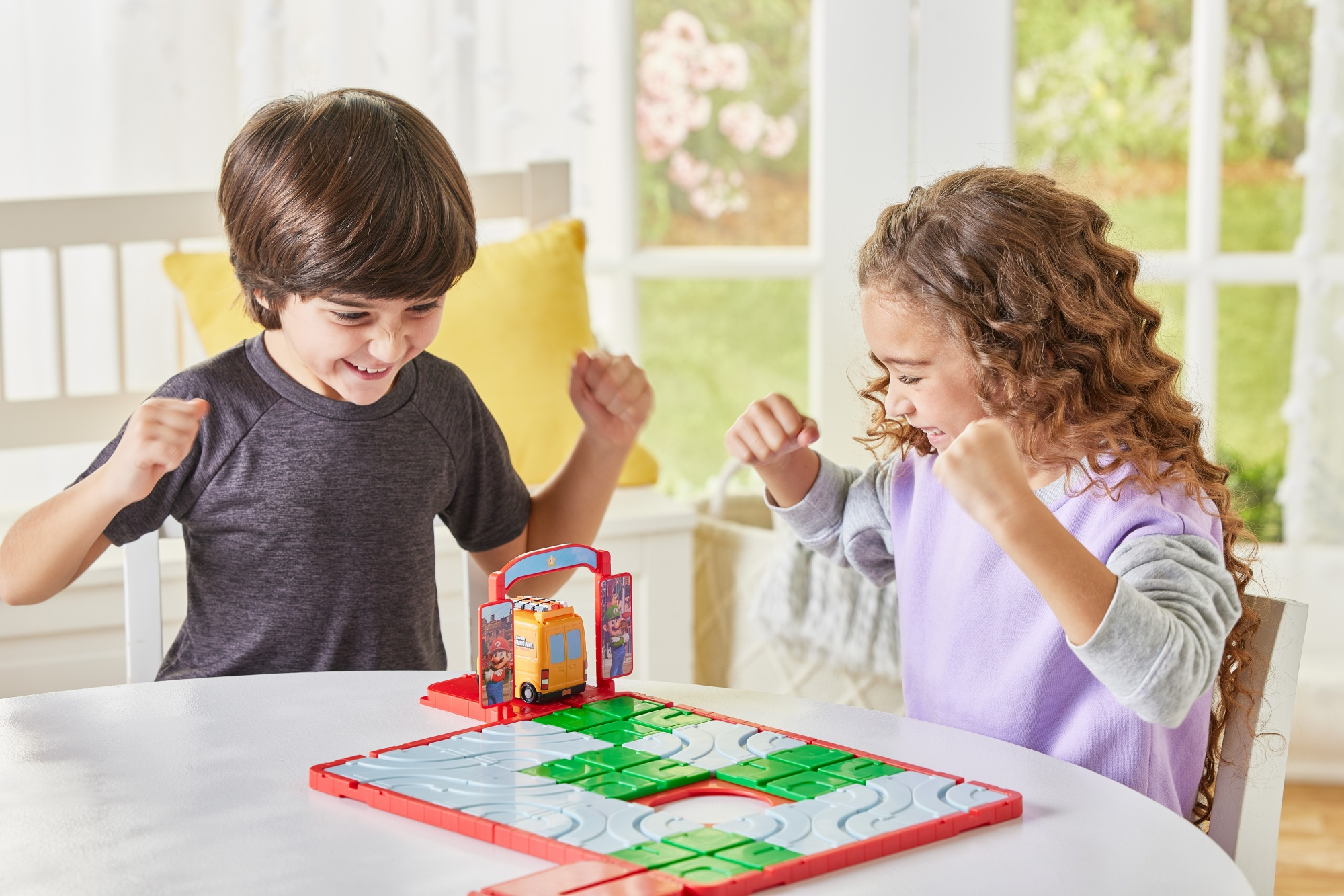 Dwoje dzieci gra w grę planszową. Chłopiec jest podekscytowany. Gra ma samochód pośrodku i zieloną ścieżkę.