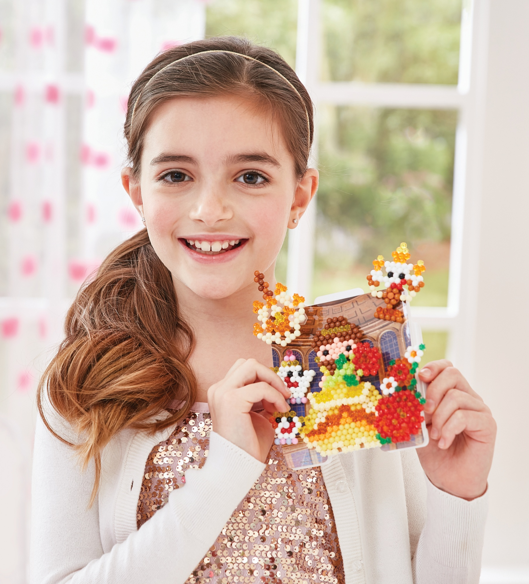 Niña sonriente sosteniendo una manualidad colorida, con un fondo blanco.