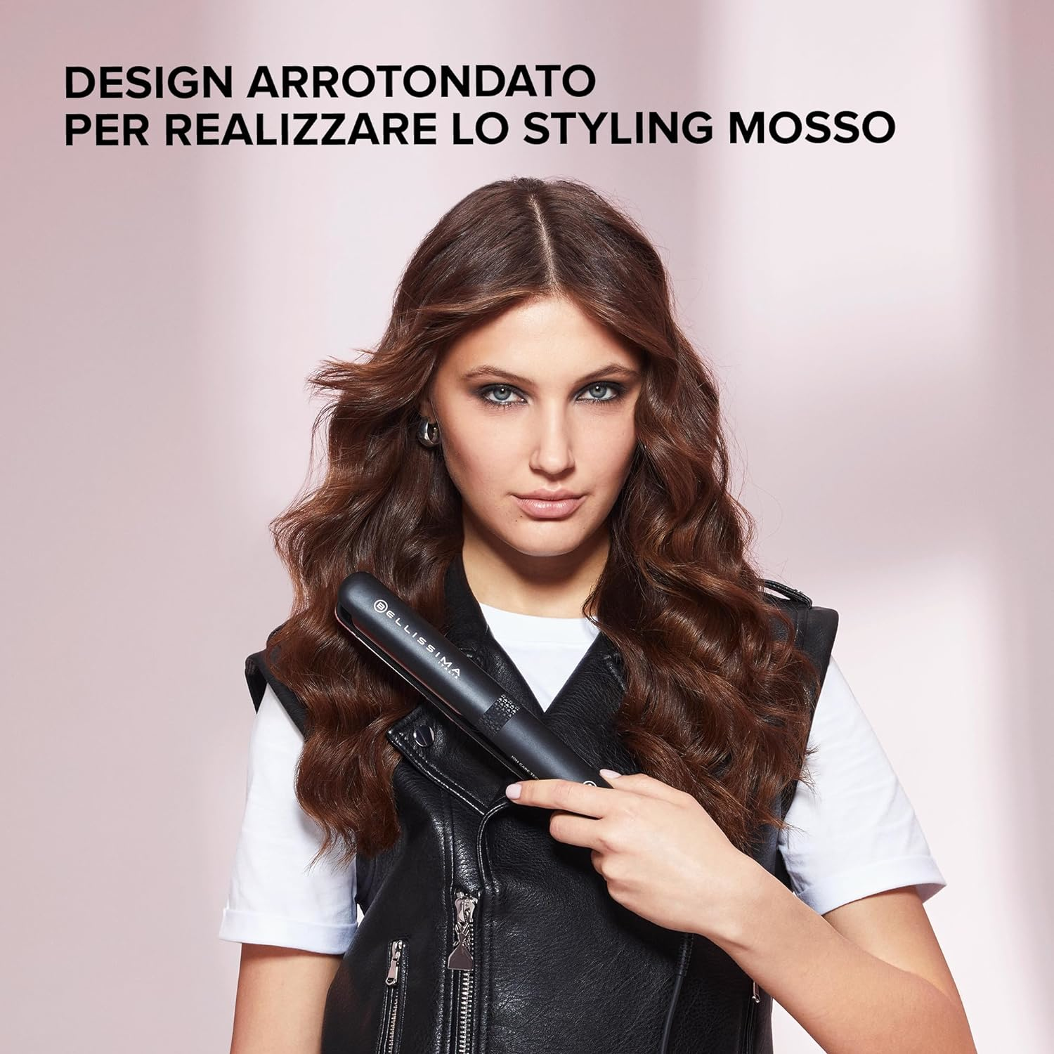 Kobieta trzymająca prostownicę. Tekst: "Zaokrąglona konstrukcja dla uzyskania falistej stylizacji." Czarna kurtka, biała koszula.