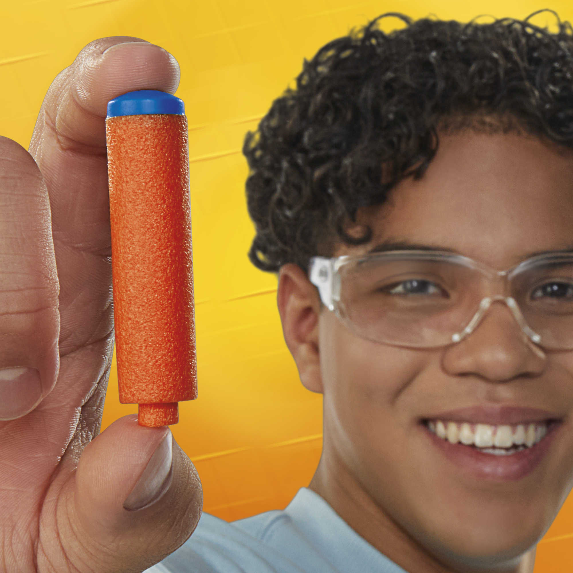 Un joven sosteniendo un dardo Nerf naranja y azul, sonriendo, con gafas de seguridad.