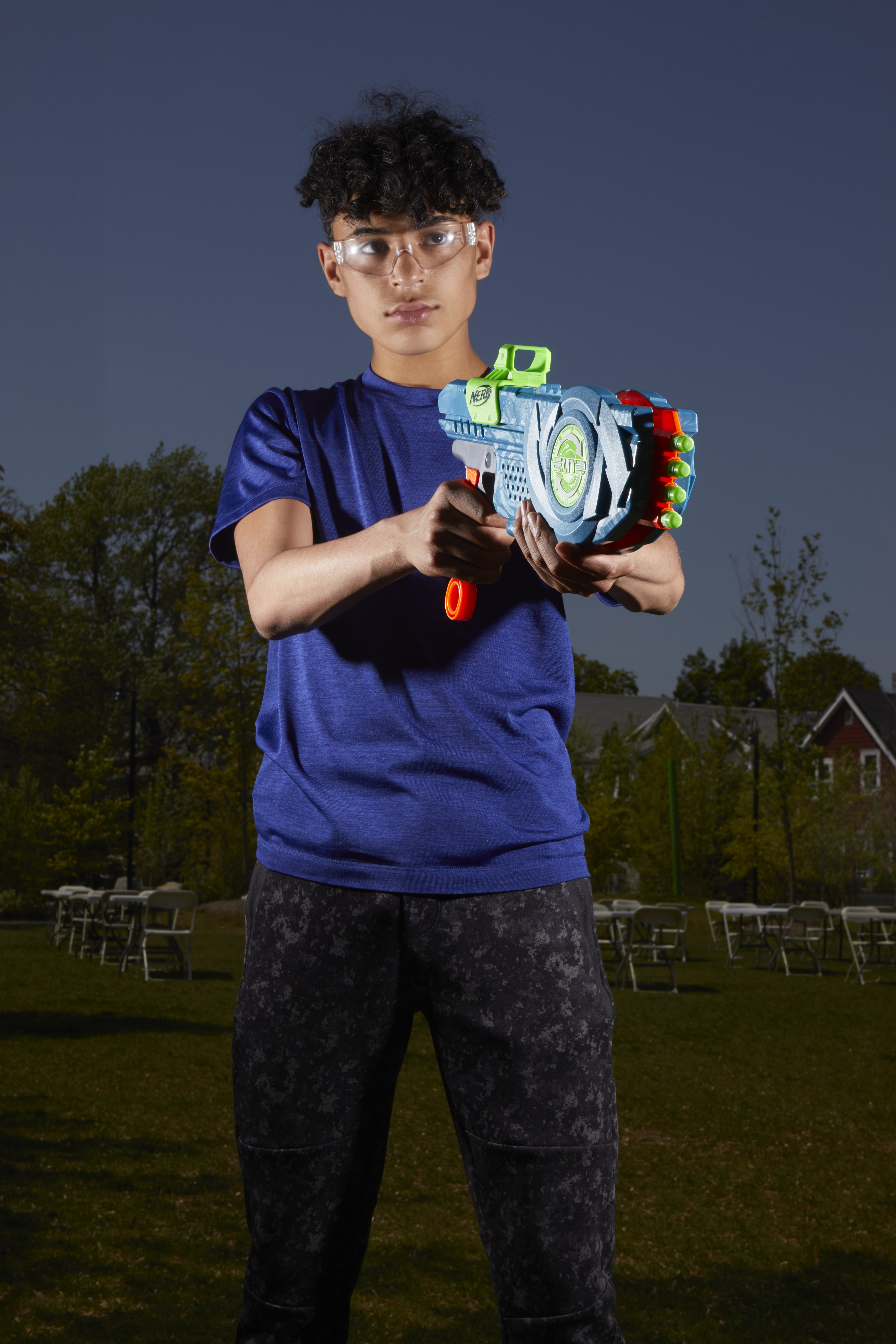 Un ragazzo che tiene una pistola Nerf, con gli occhiali, in piedi fuori con alberi sullo sfondo.