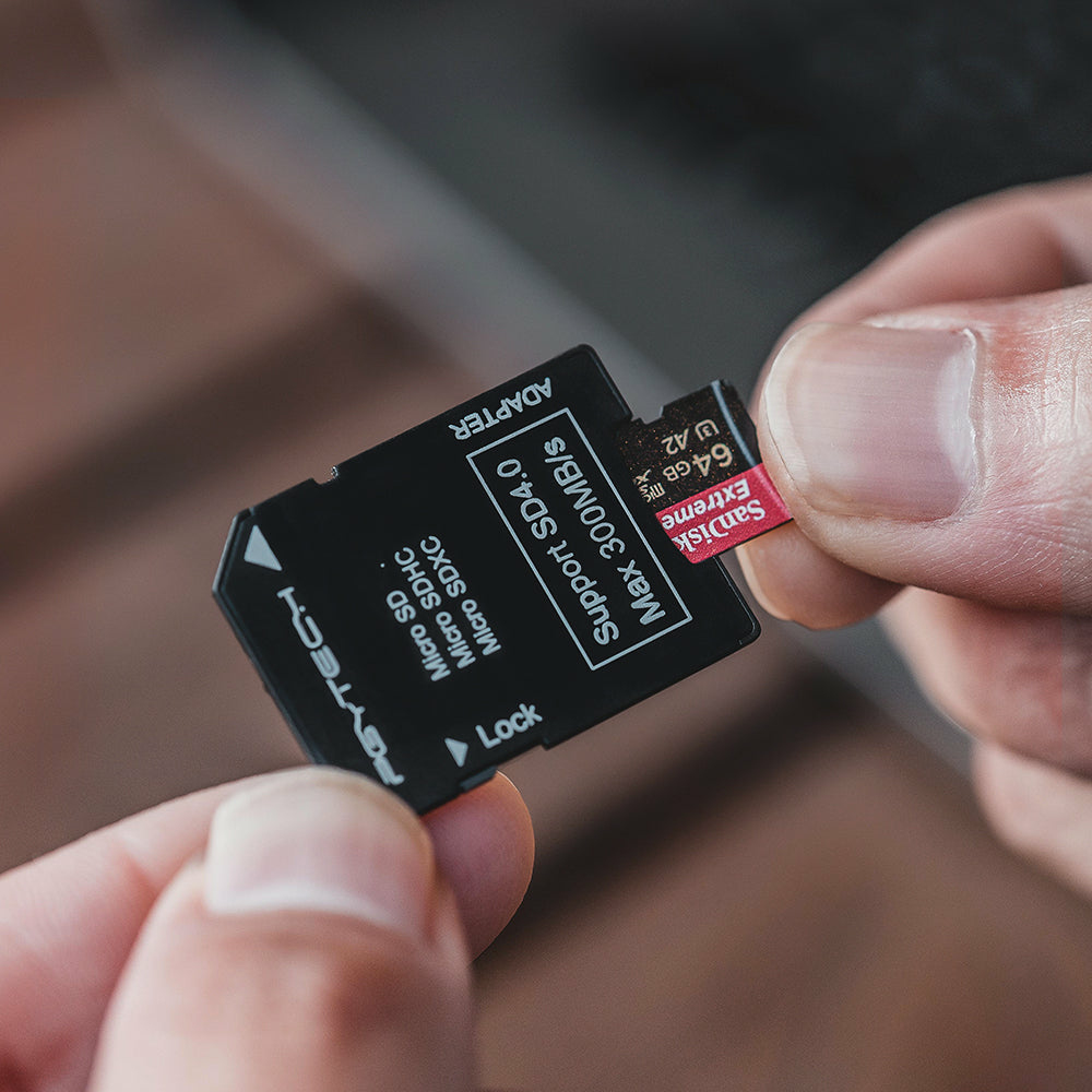 Osoba trzymająca czarną kartę SD. Karta SD jest włożona do czarnego adaptera. Karta odczytuje 64 GB.