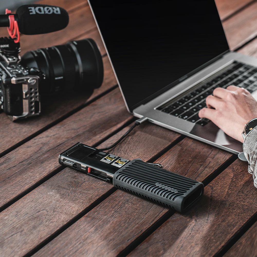 Laptop, rejestrator i aparat na drewnianym stole. Ręka używa laptopa.