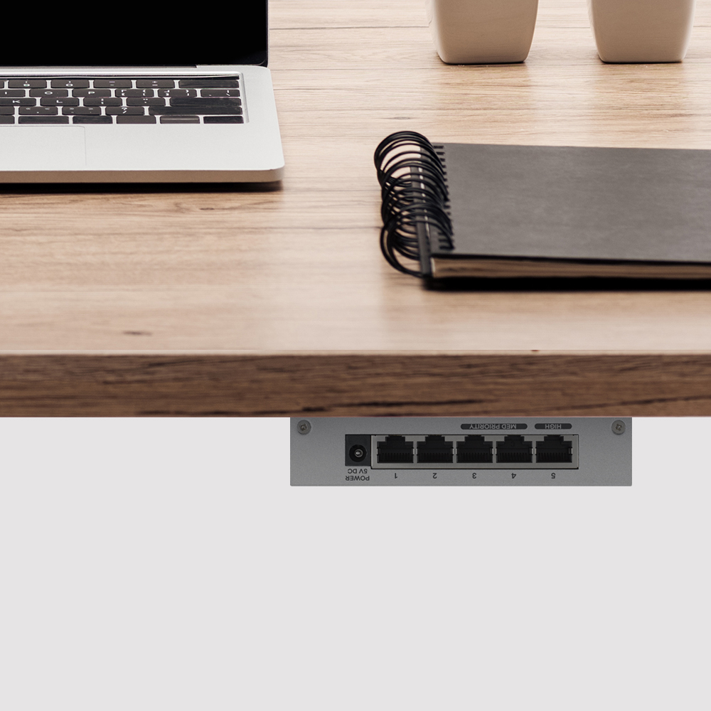 Laptop, notebook e switch di rete su una scrivania di legno.