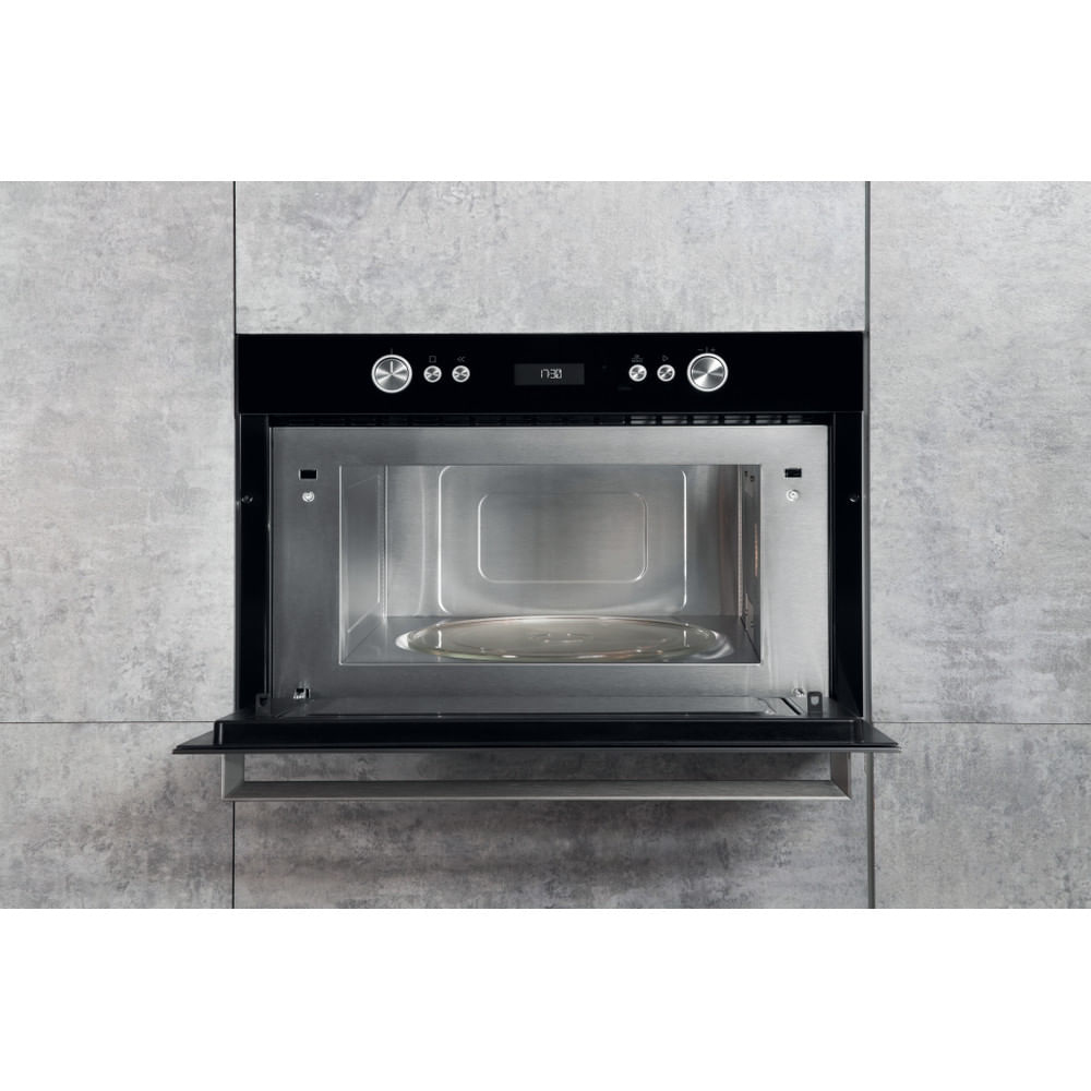 Microonde nero con porta aperta, interno in acciaio inox, su muro grigio. Display mostra 1:30.