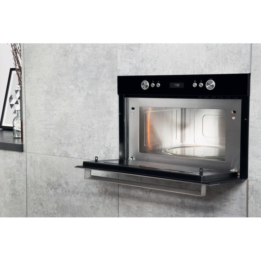Un forno a microonde nero è montato su una parete piastrellata grigia. La porta è aperta e l'interno è visibile.