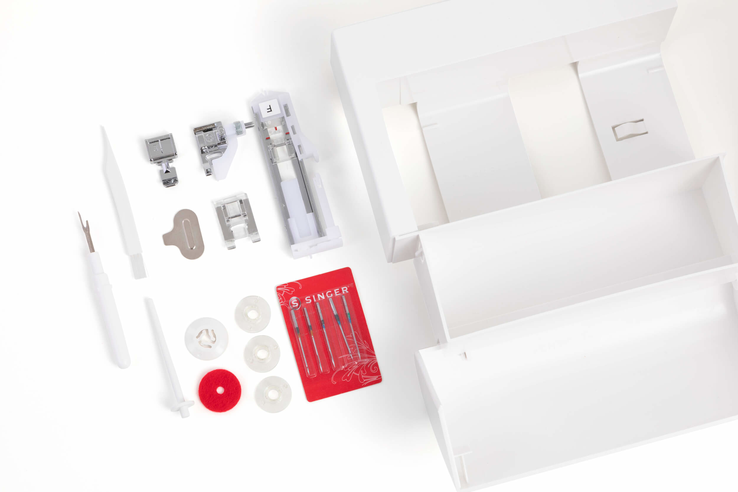 Akcesoria do maszyn do szycia, igły i części, starannie ułożone w otwartym białym pudełku.
