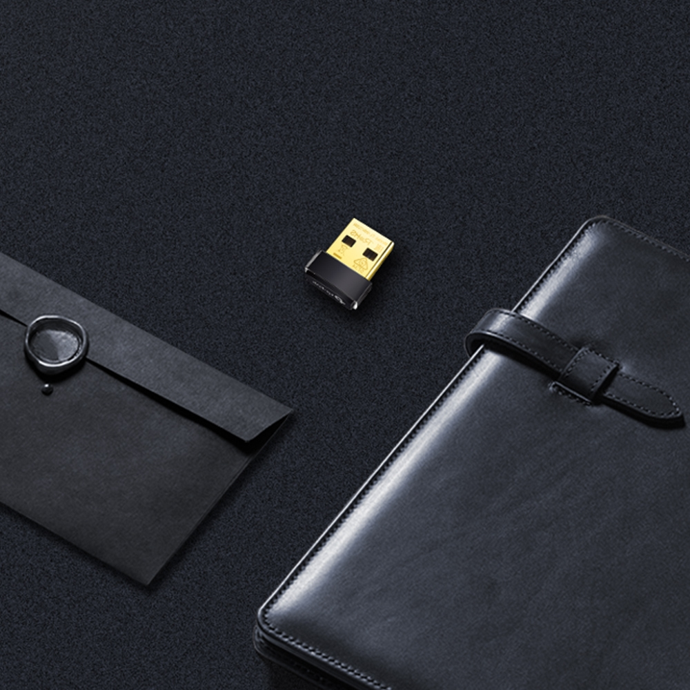 Un receptor USB junto a un cuaderno negro y un sobre, todo sobre una superficie oscura y texturizada.
