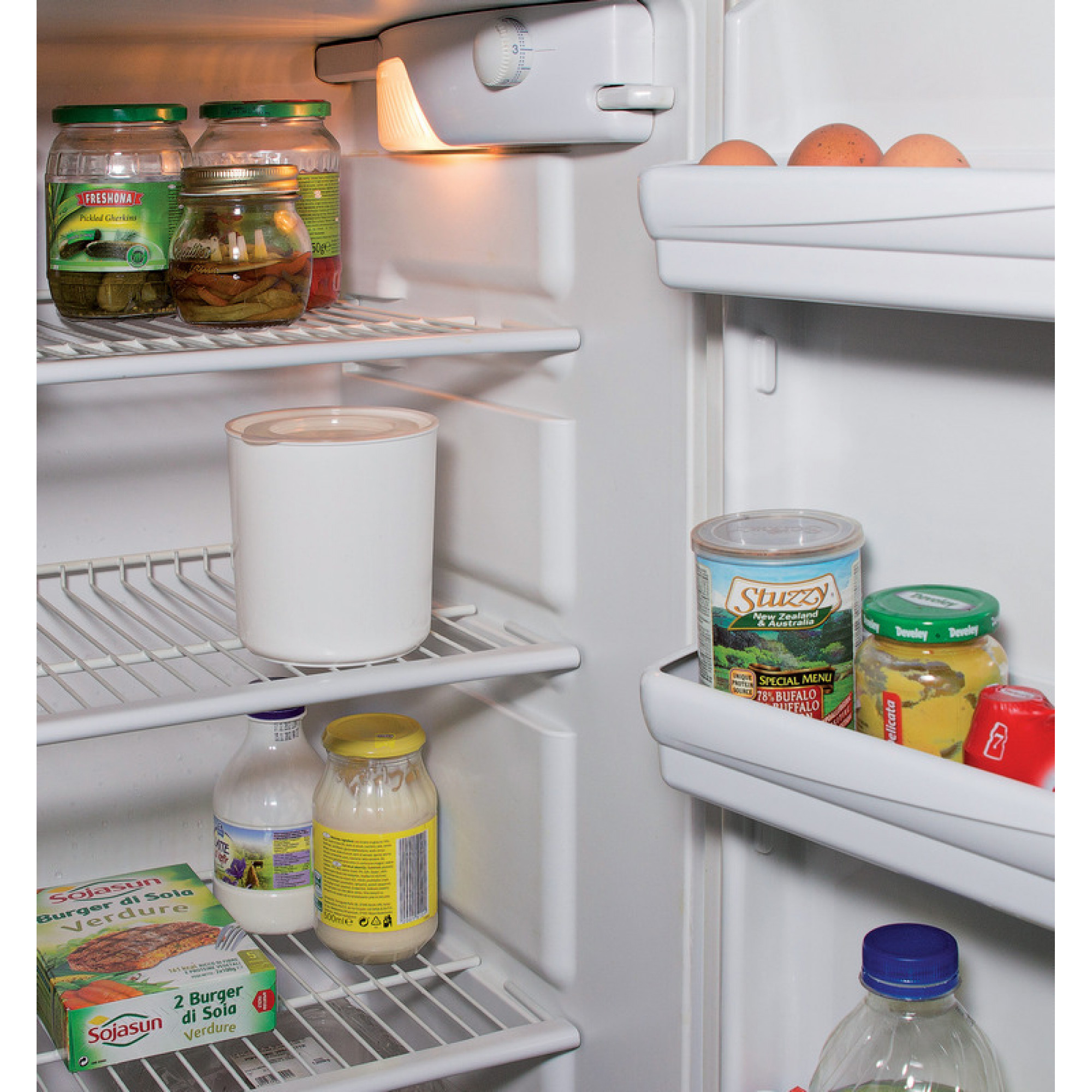 Wnętrze lodówki ze słoikami, białym pojemnikiem, mlekiem i pudełkami z żywnością. Jajka na górnej półce.