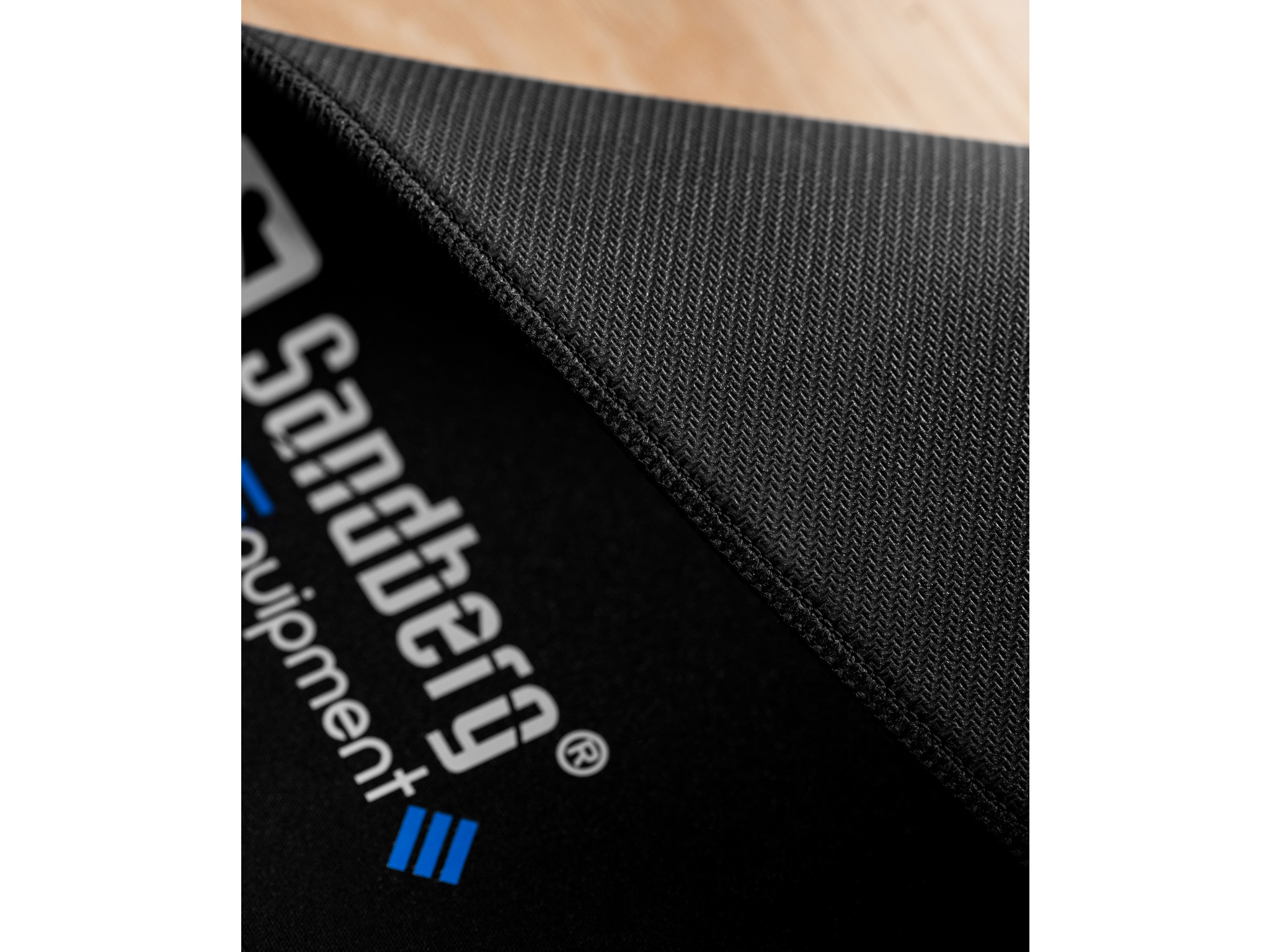 Gros plan d'une surface noire texturée avec le logo Sandberg en diagonale. La texture est légèrement visible.